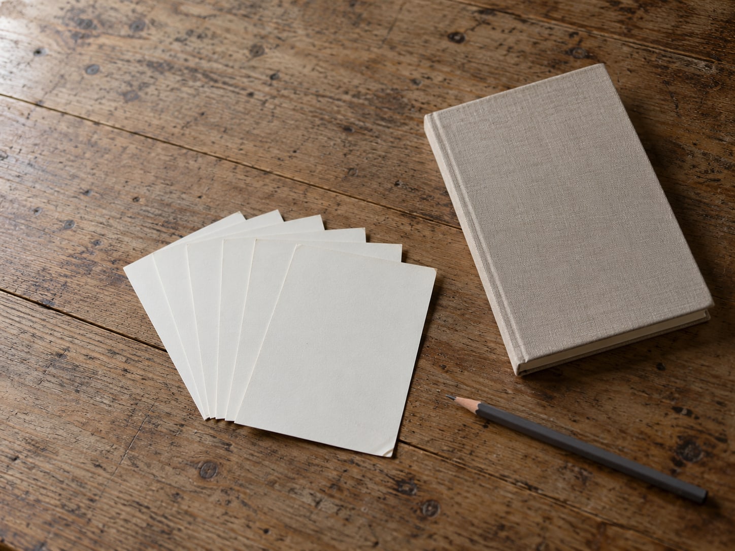 Six blank index cards fanned out on a wooden desk beside a closed notebook and a pencil.