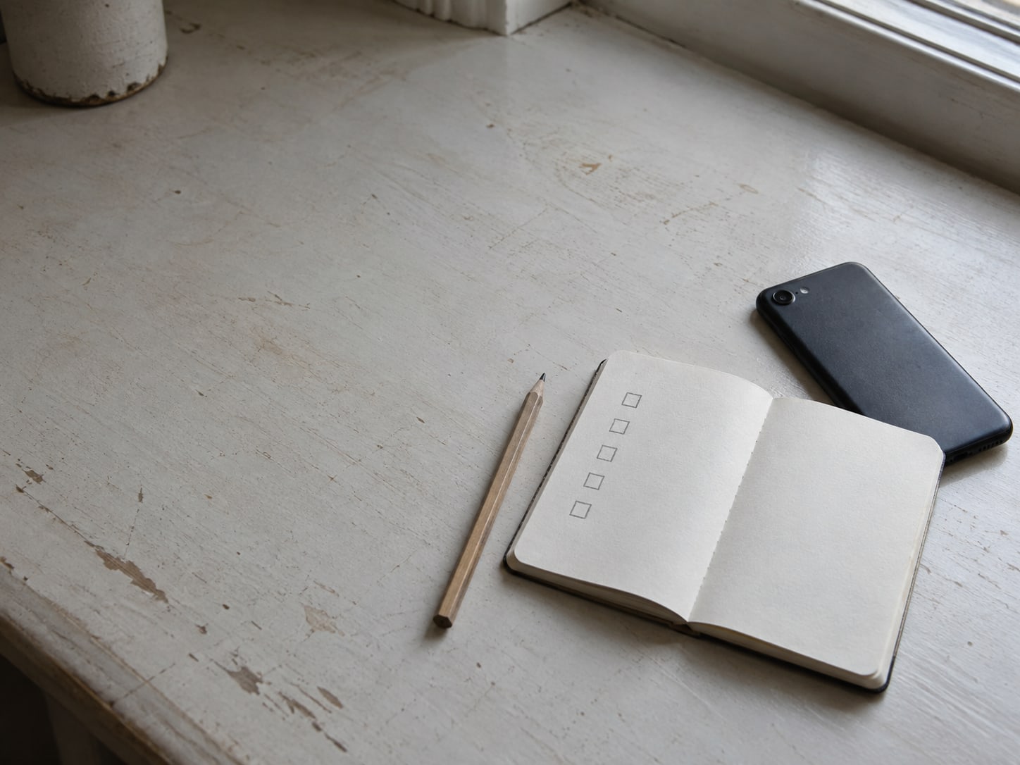 A small notebook open to a pencil-drawn checklist of boxes, beside a closed phone and a pencil.