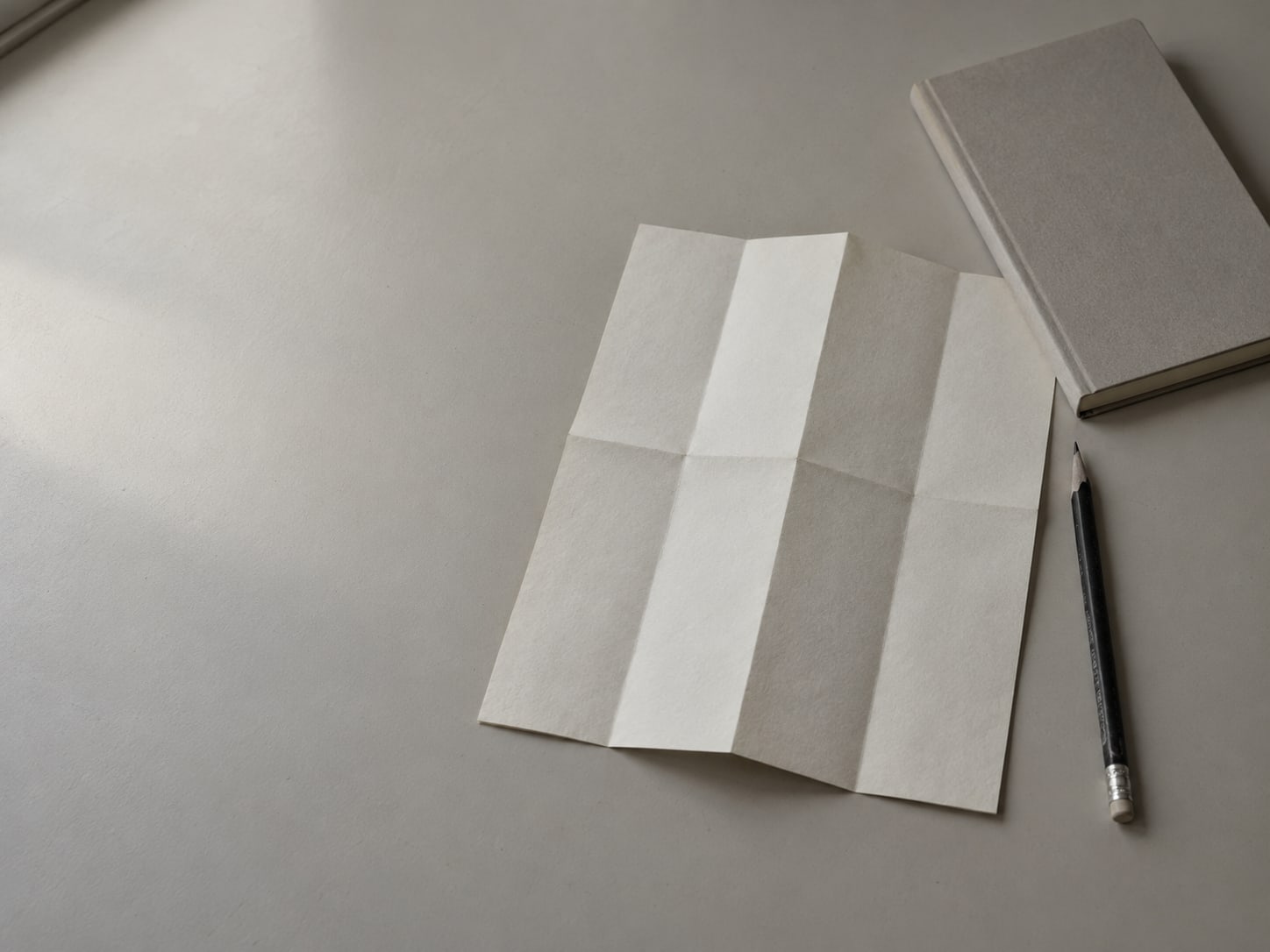 A folded blank paper map and a pencil resting on a clean desk beside a closed notebook.