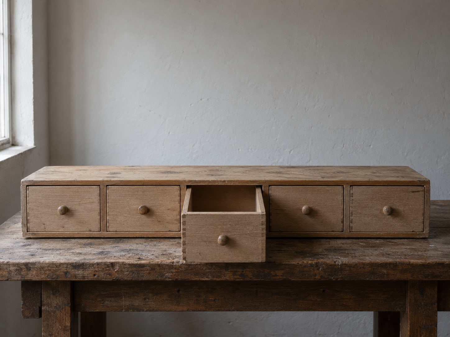 A tidy row of wooden drawers with one drawer pulled open and empty on a workshop bench.
