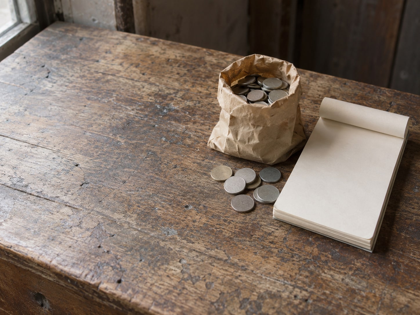 A small paper bag of loose coins beside a blank receipt pad on a worn counter.