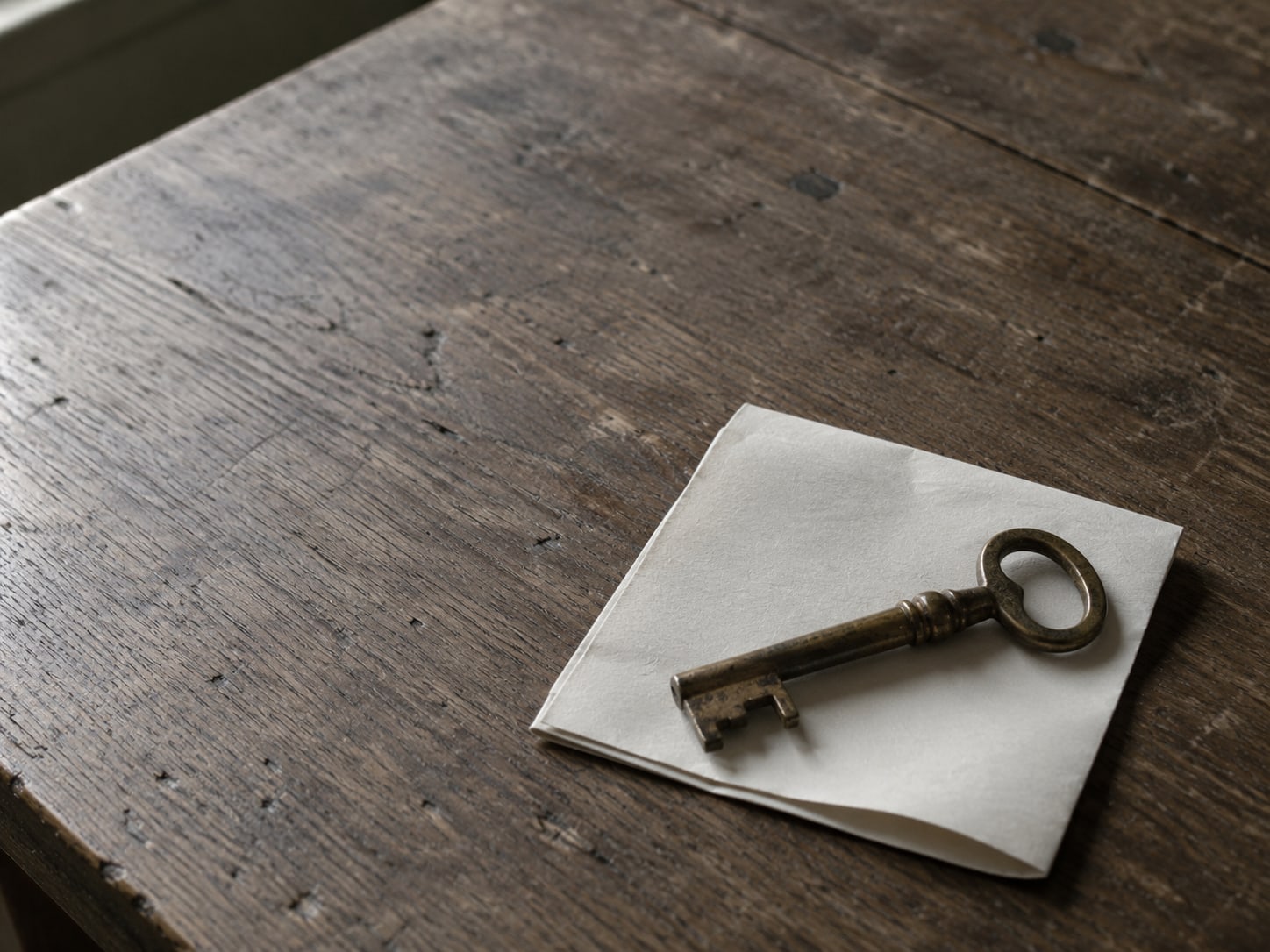 A single brass key resting on a folded blank sheet of paper on a wooden desk.