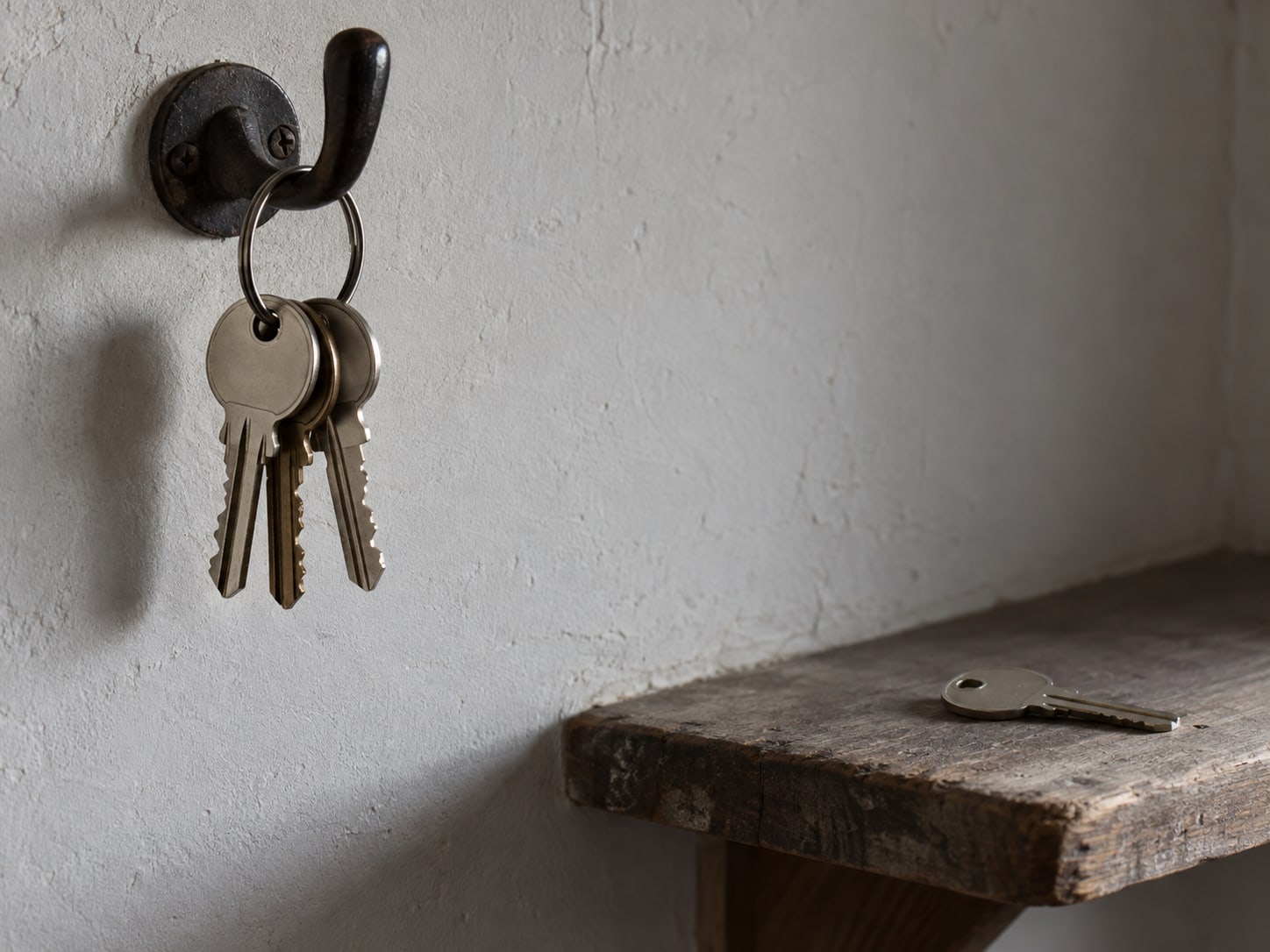 A ring of house keys on a hook beside one spare key on a small shelf in a quiet entryway.