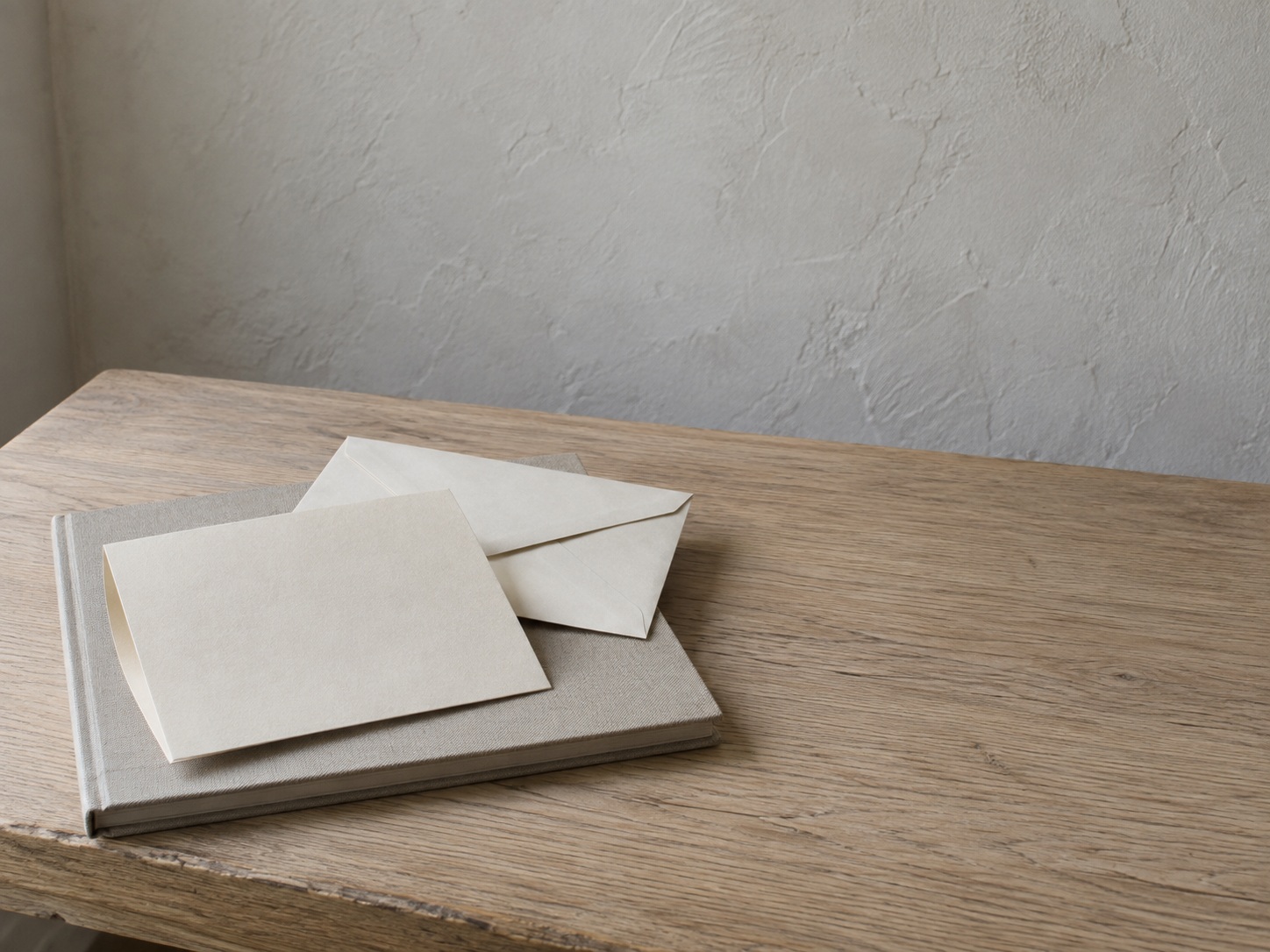 A folded sheet of blank paper and a sealed envelope resting on a closed notebook on a light oak table.
