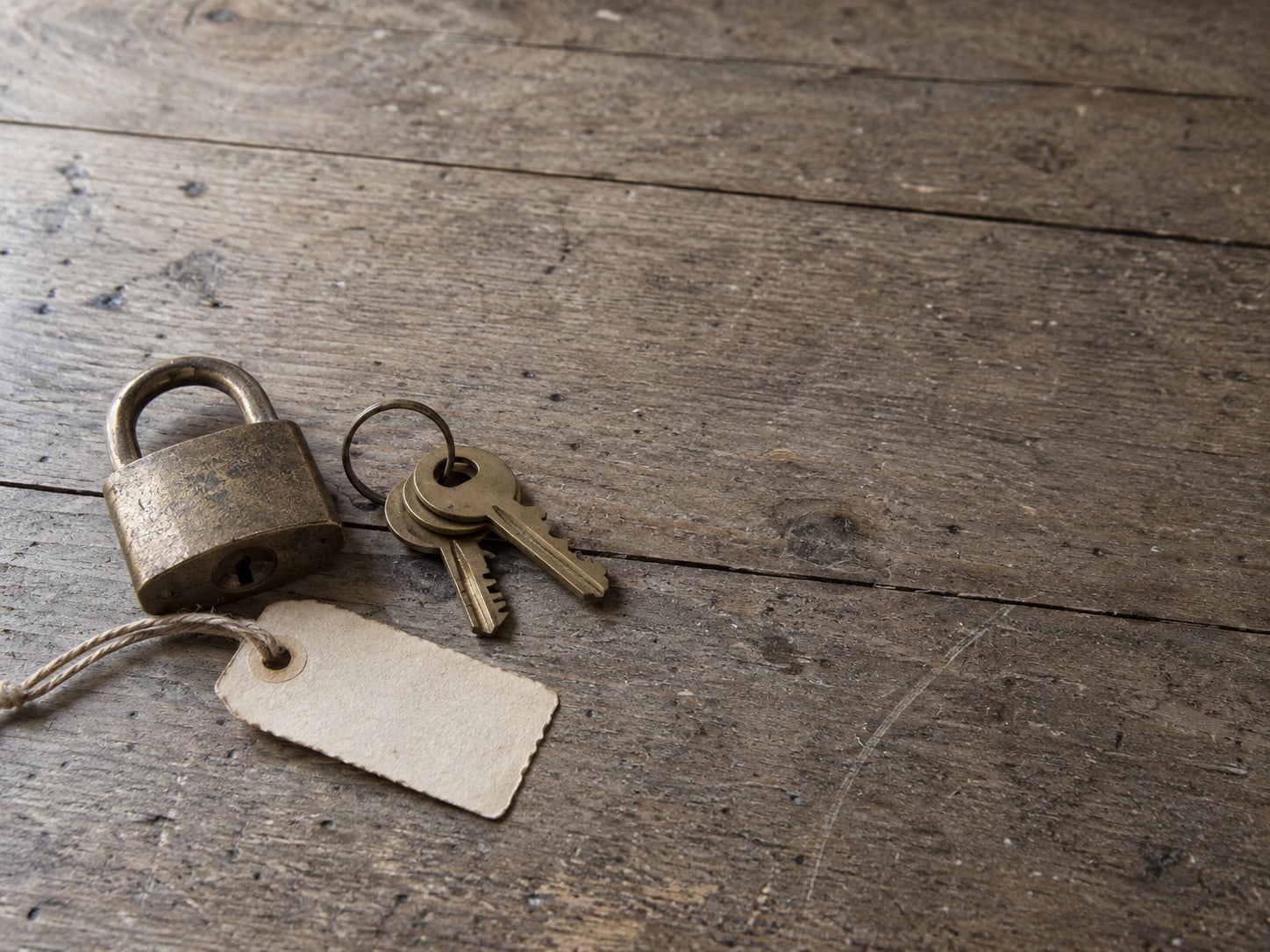 A flat lay of a small brass padlock, a ring of keys and a blank paper tag on a worn wooden desk.