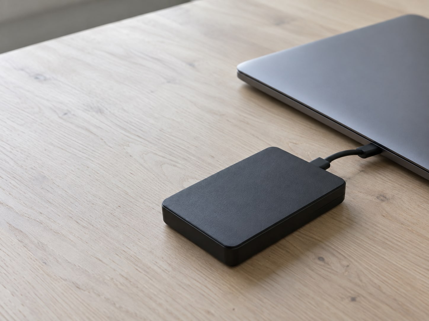 Un disco duro externo pequeño junto a una laptop cerrada, sobre un escritorio limpio.