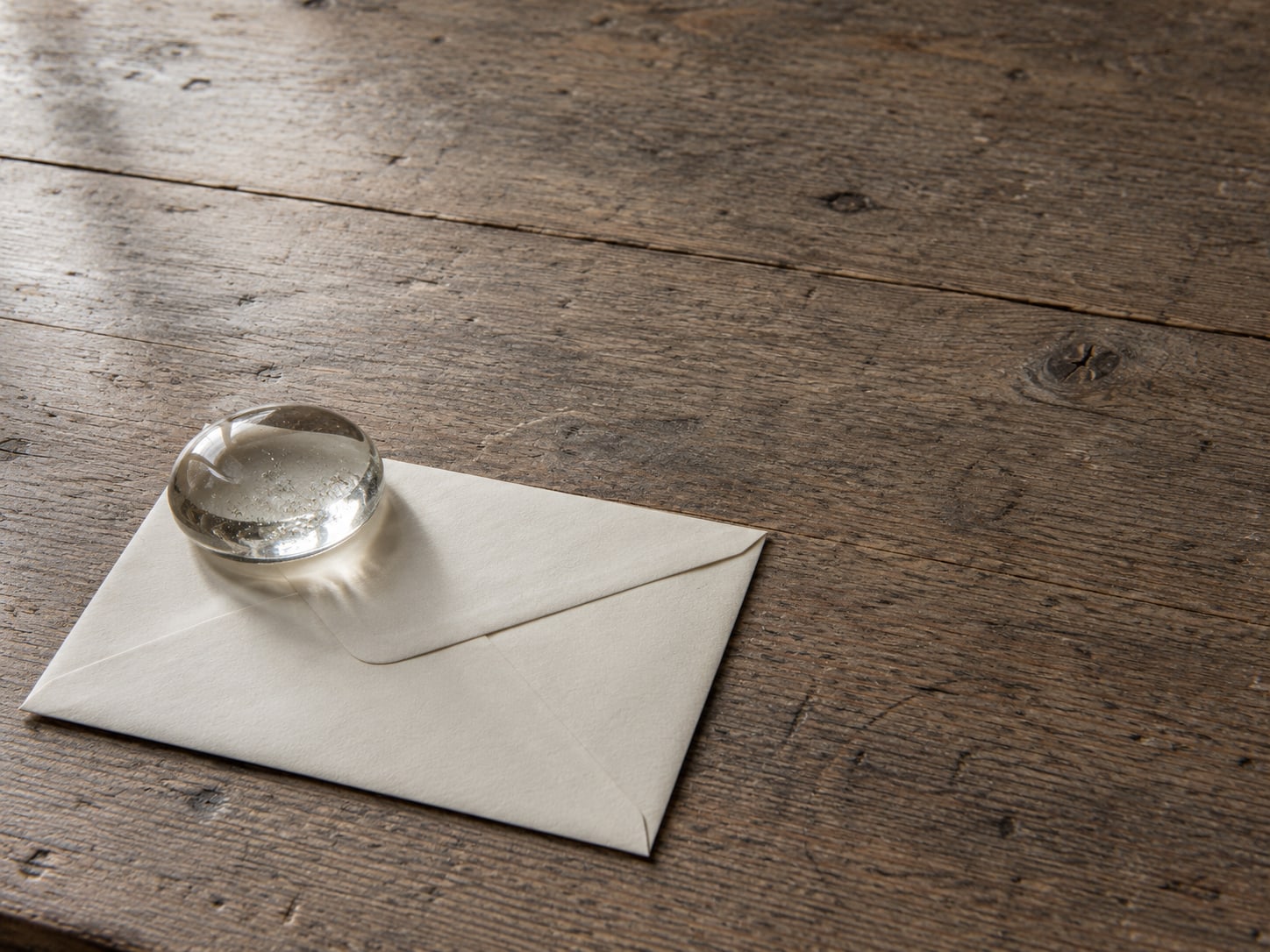 A sealed envelope held down by a small glass paperweight on a clean wooden desk.