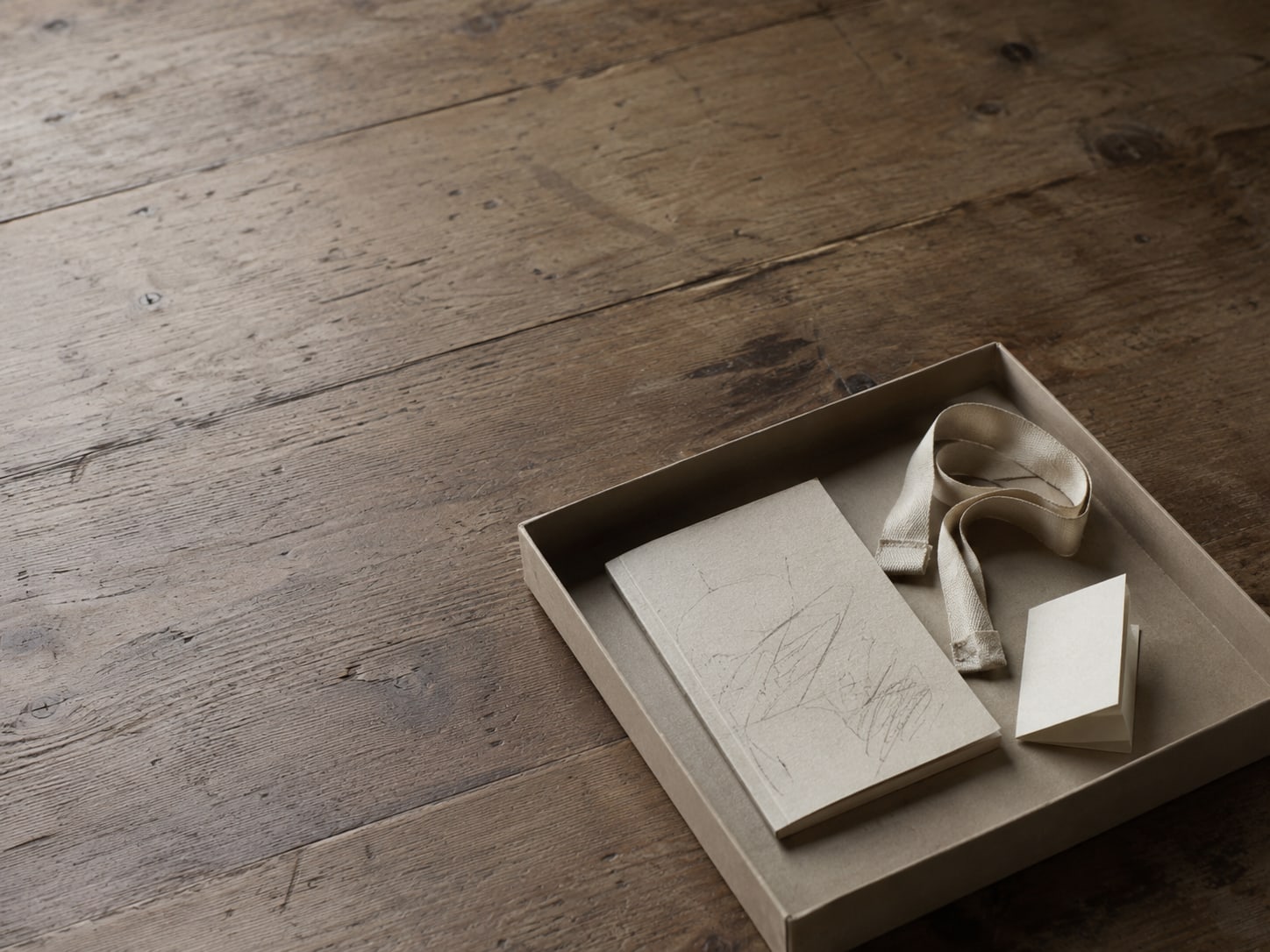 A shoebox lid holding a small notebook with pencil notes, a tape measure and a folded care tag on a wooden table.