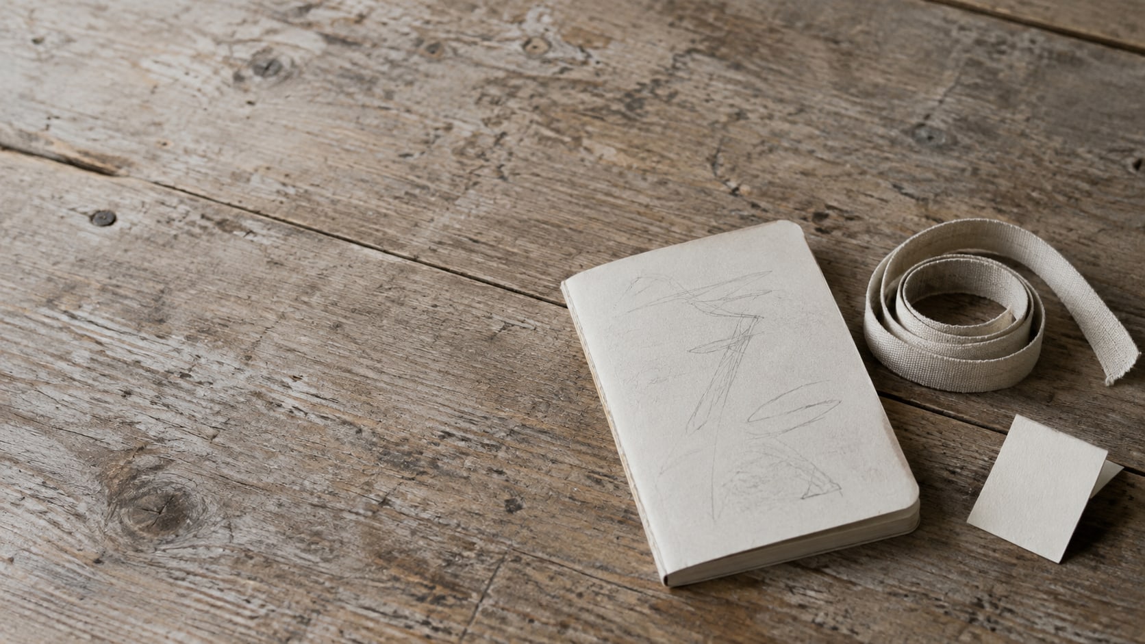 A small notebook with pencil notes, a tape measure and a folded blank care tag laid out on a wooden table.