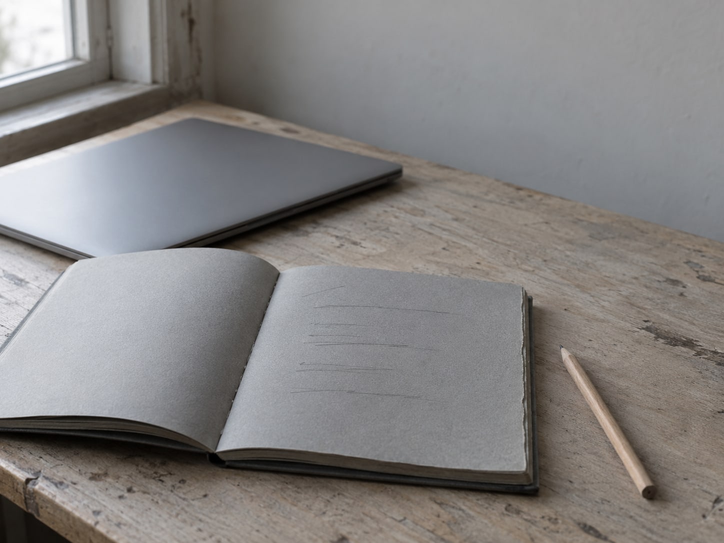 A notebook with a short handwritten list of items sits open on a desk next to a closed laptop and a pen.