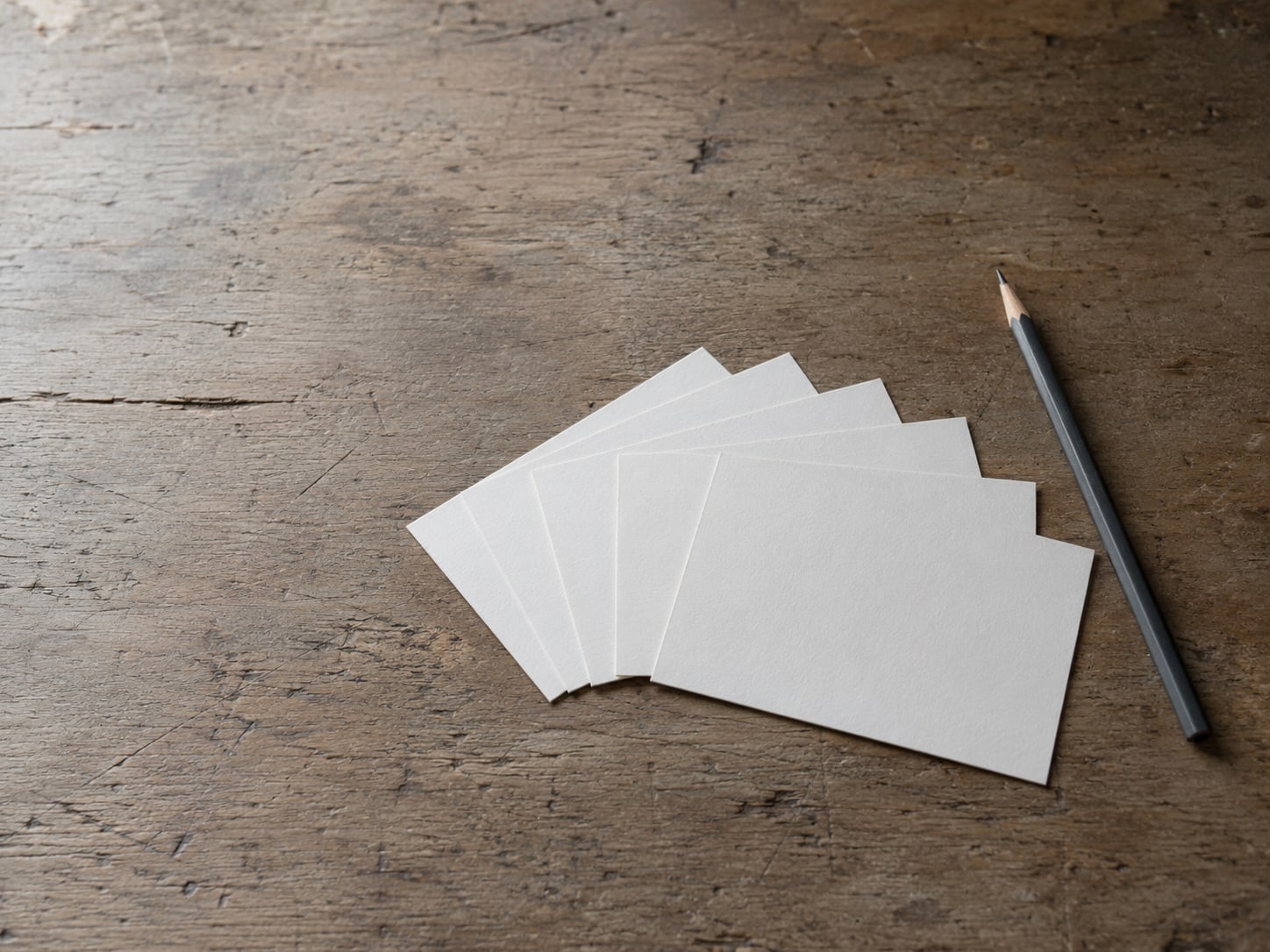 Five blank index cards fanned out on a desk beside a pencil.