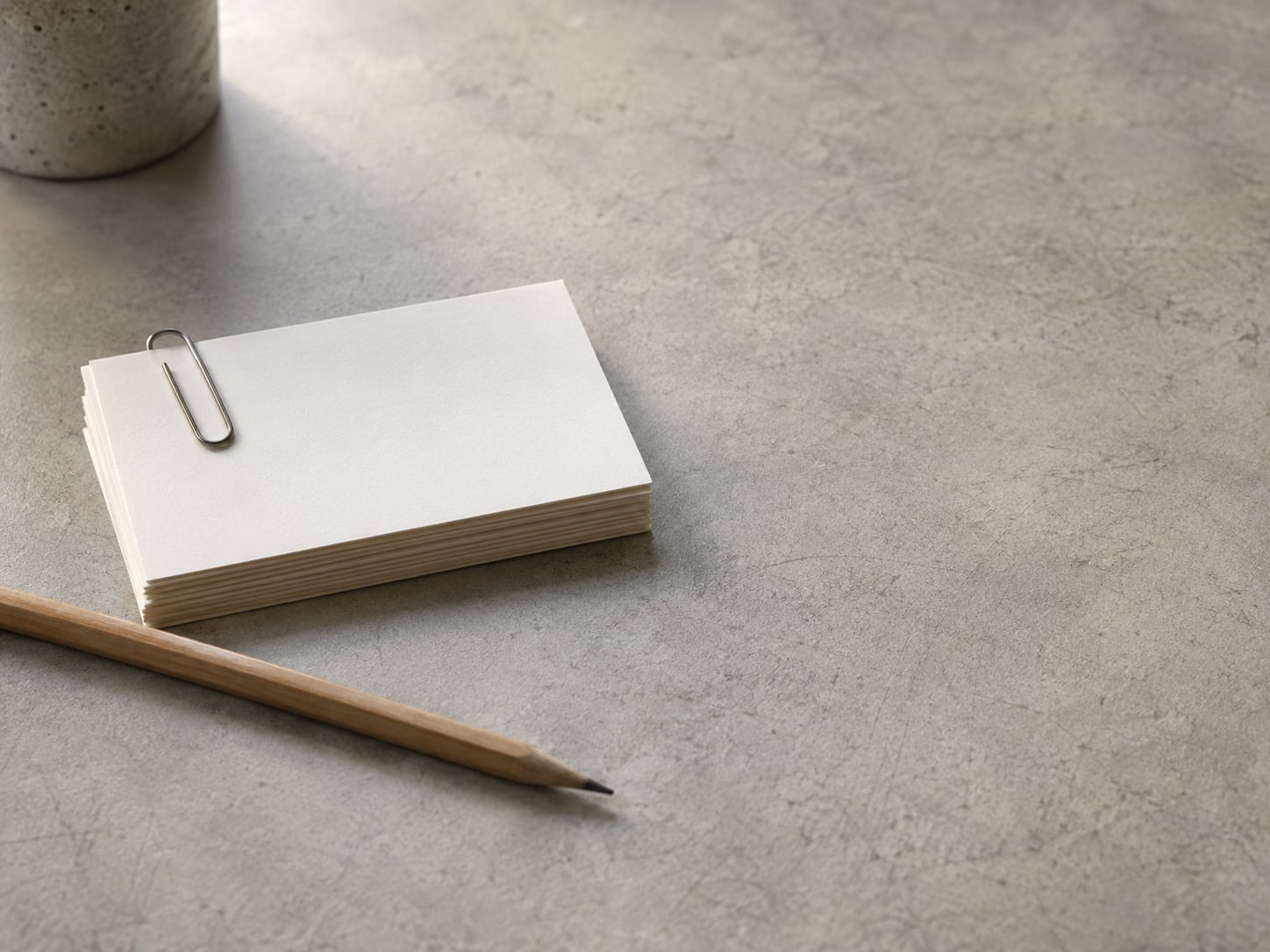 A small stack of blank index cards held with a paper clip beside a pencil on a plain desk.
