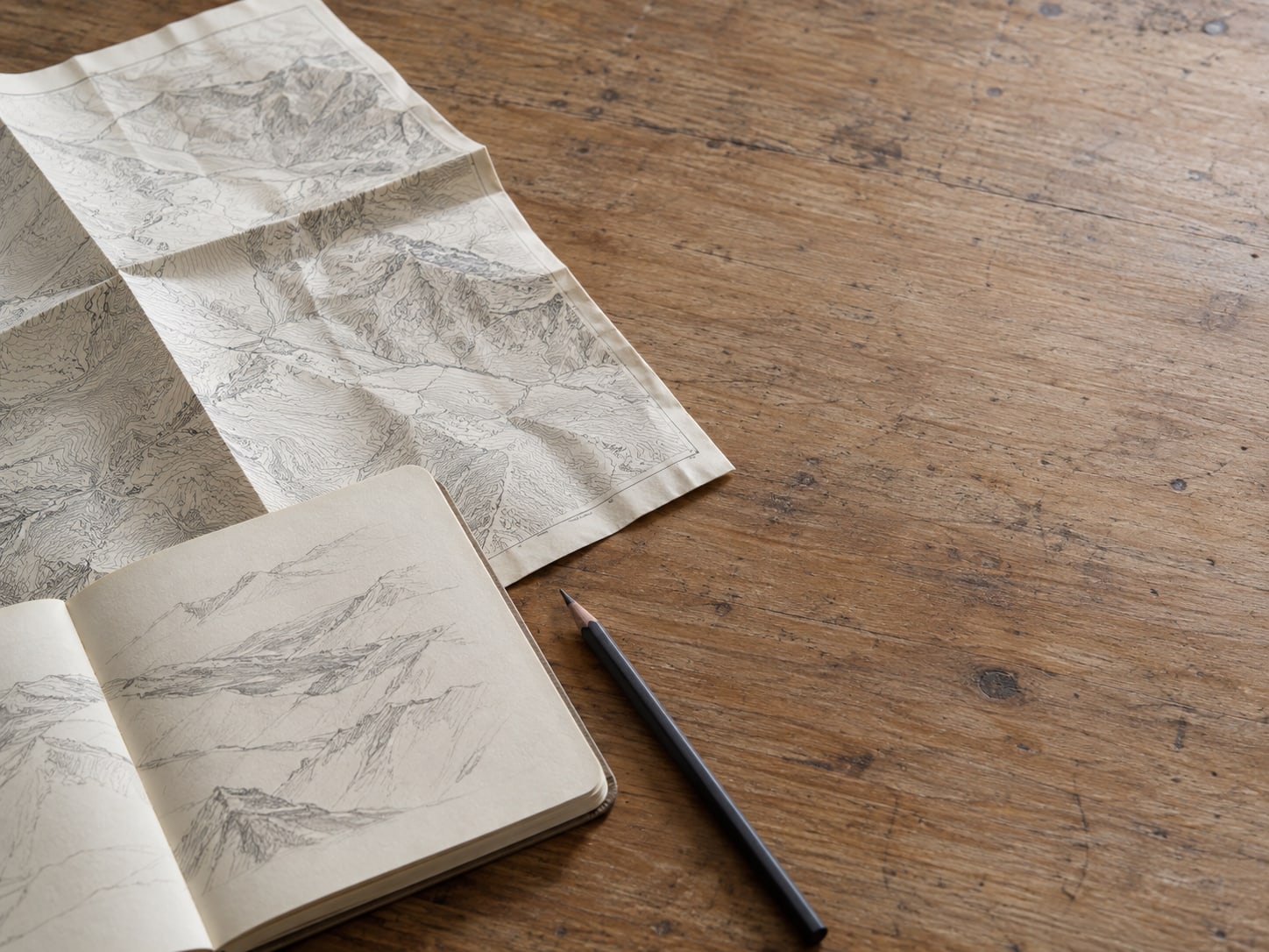 A wooden desk with a paper map folded open, a pencil and a small notebook with unreadable pencil marks.