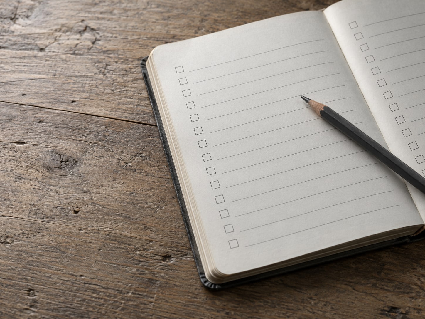 A worn notebook open to a page of blank checkbox lines, with a pencil resting across it.