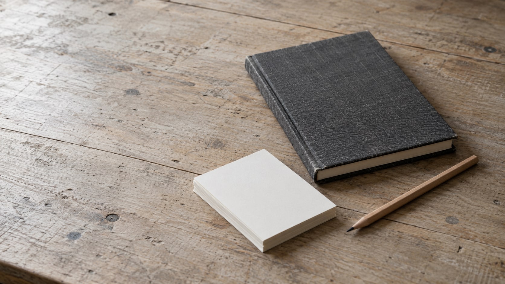 Un cuaderno cerrado, un lápiz y una pila de fichas en blanco sobre un banco de trabajo.