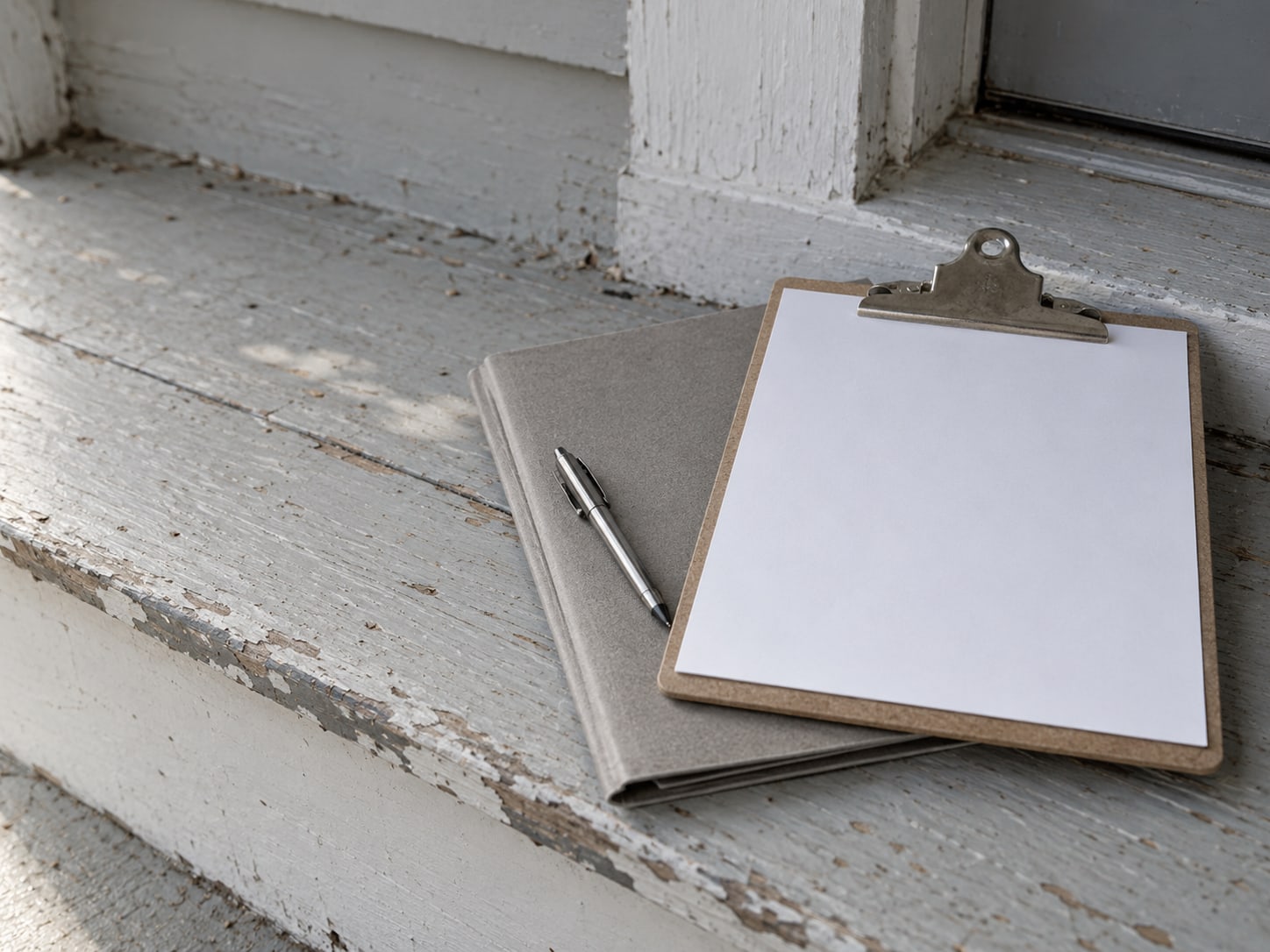 A blank clipboard with a pen on top of a closed folder, resting on a painted porch step.