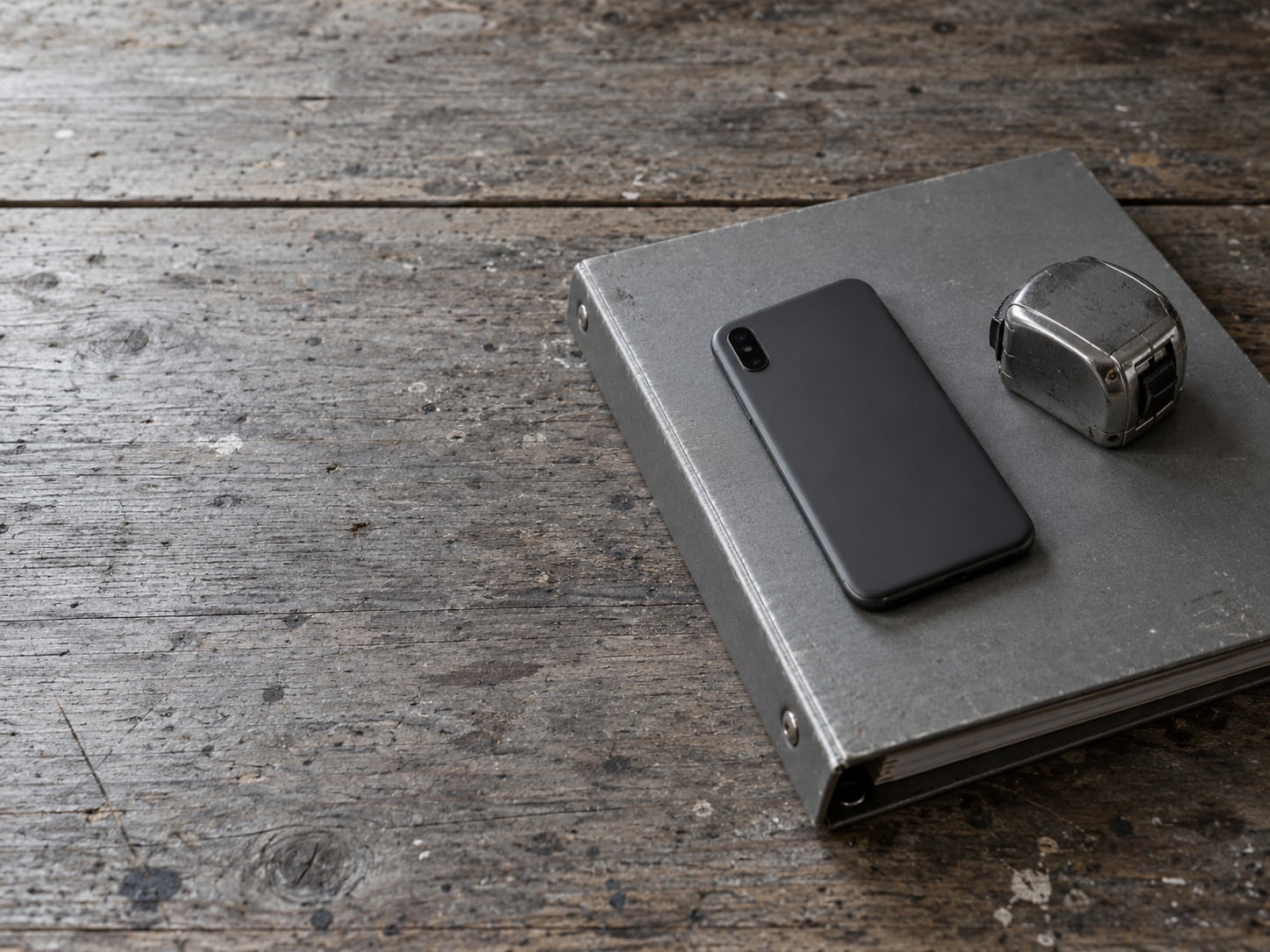 A closed smartphone lying face down on a three-ring binder beside a tape measure on a workbench.
