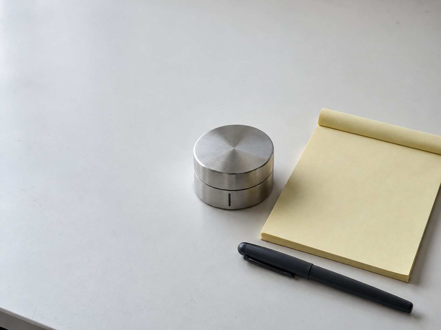 A small kitchen timer beside a blank yellow legal pad and a capped pen on a white desk.