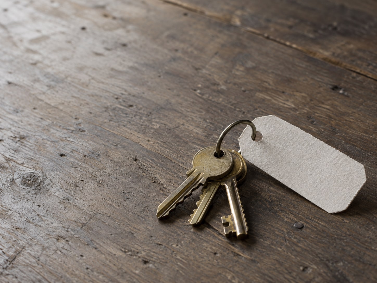 A ring of brass keys on a worn wooden table beside a blank paper tag.