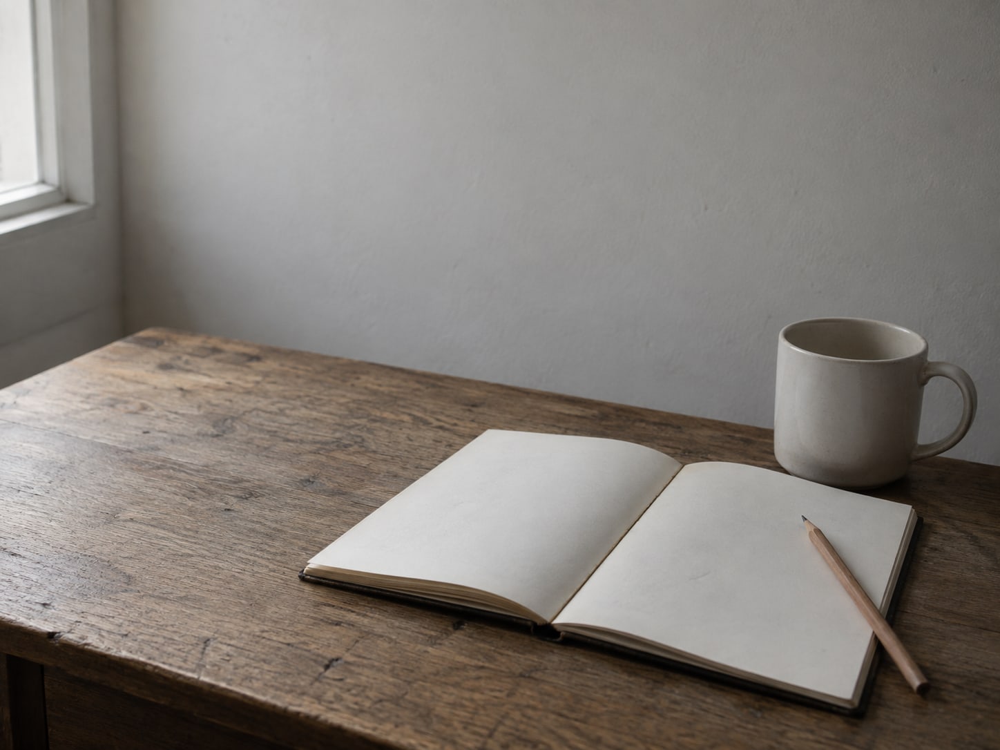 An open notebook with faint unreadable pencil marks beside a sharpened pencil and a ceramic mug on a desk.