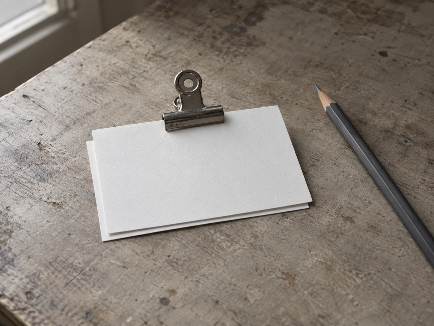 A small stack of blank index cards held with a metal clip beside a pencil on a desk.