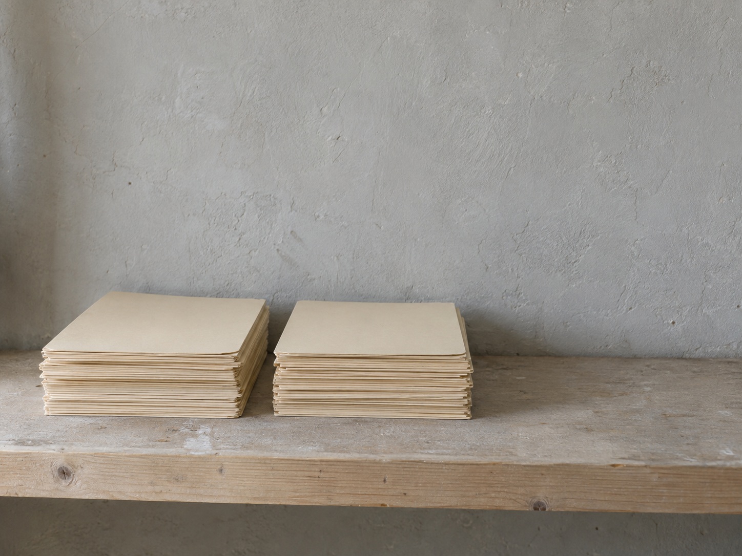 Two neat stacks of plain manila folders, one slightly apart from the other, on a light wooden shelf.