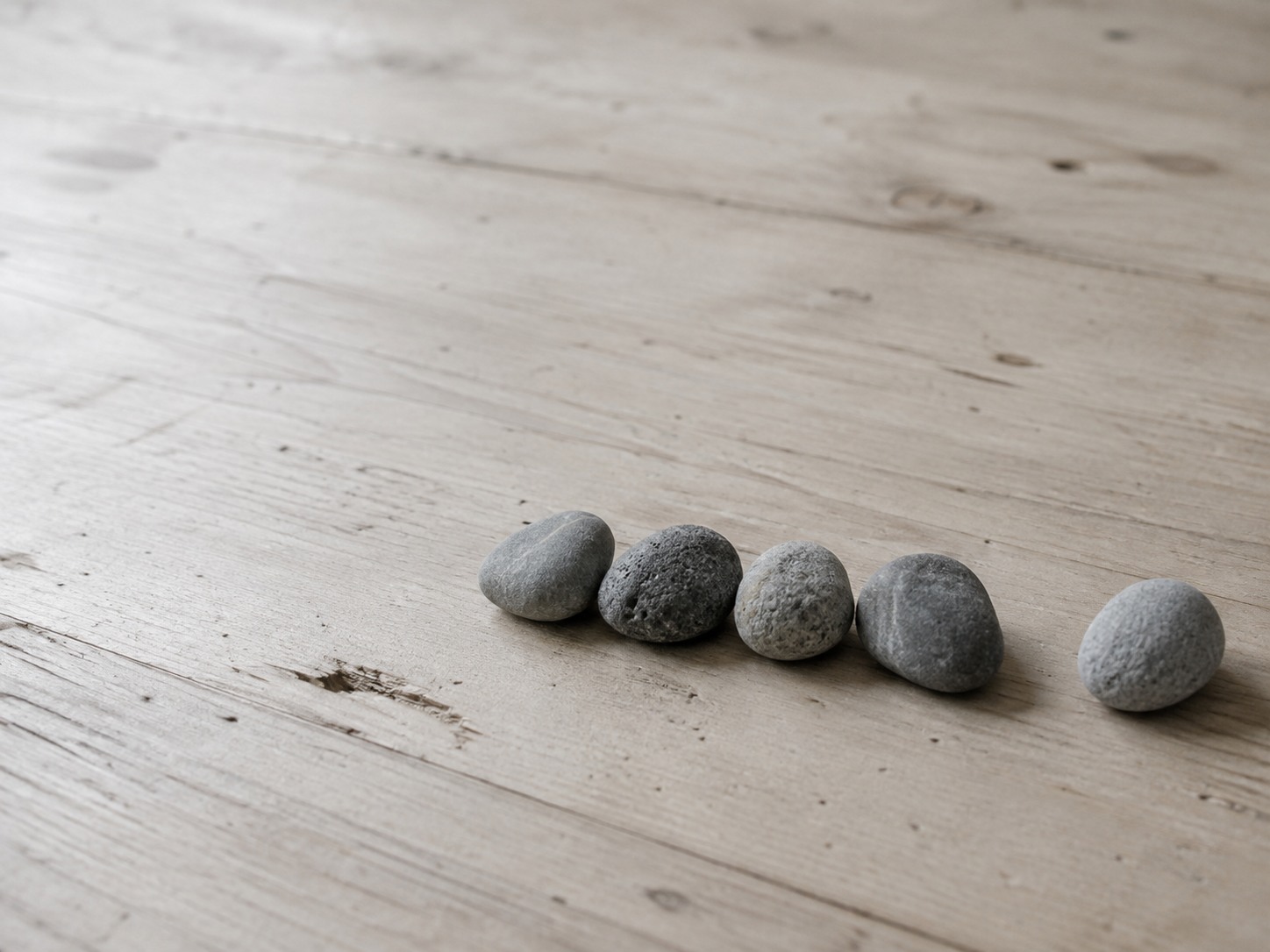 Five small smooth gray stones laid in a row on a pale wooden surface, with one stone set slightly apart from the others.