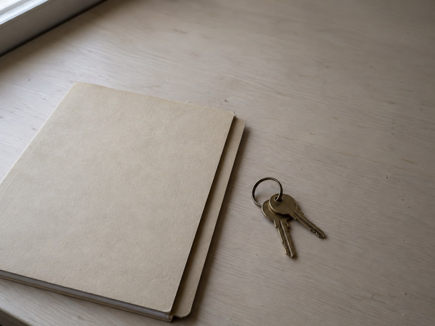 A ring with two brass keys resting beside a closed folder on a clean desk.