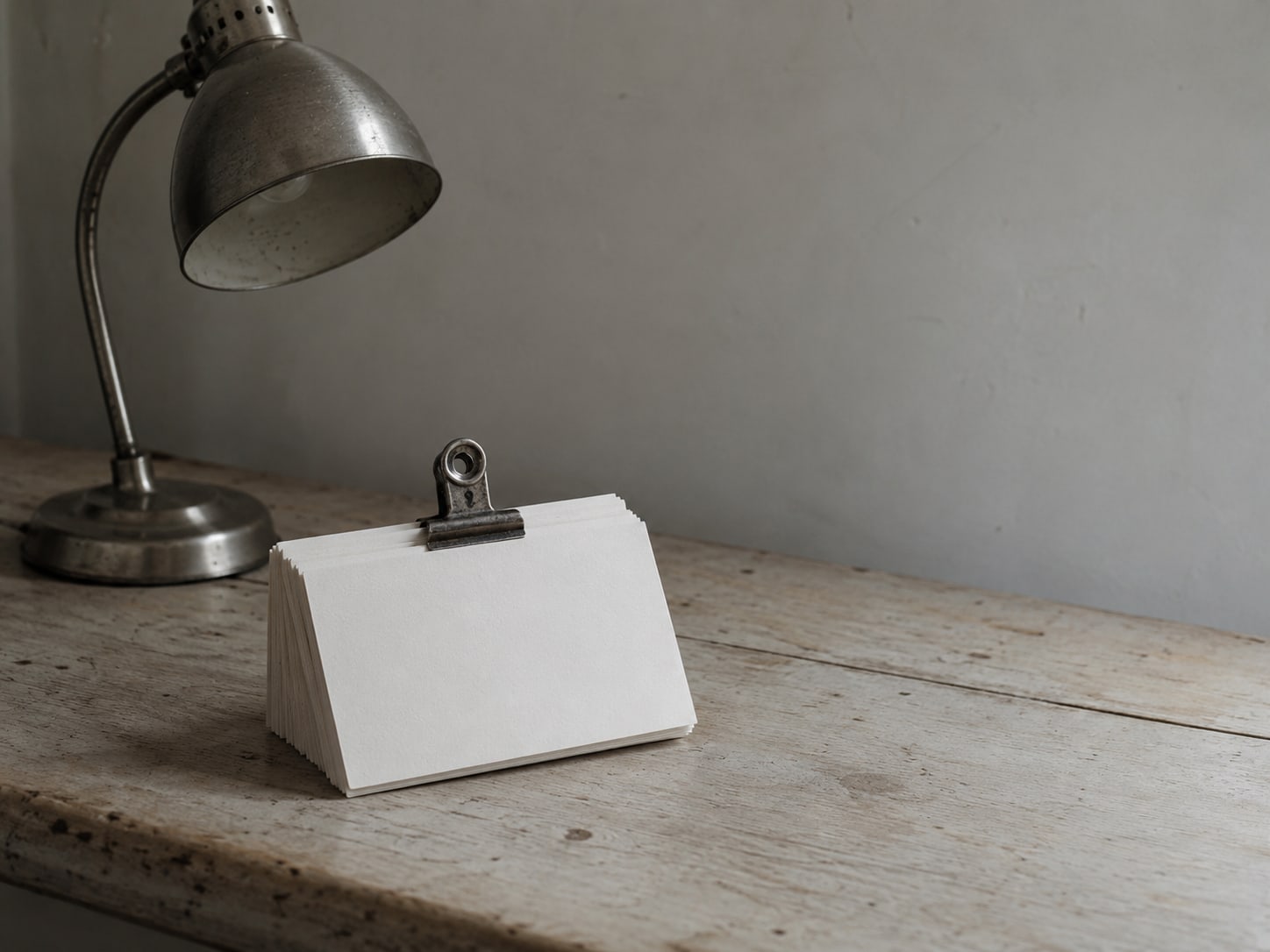 A stack of plain index cards held together with a metal clip beside a small desk lamp.