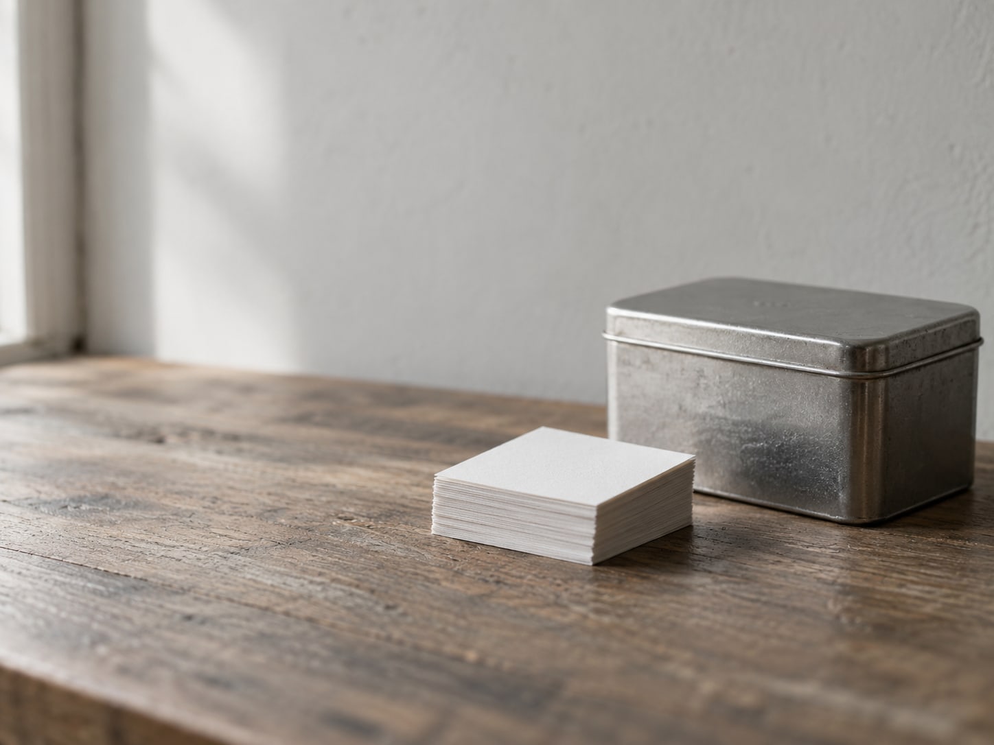 A small stack of blank paper coupons squared up on a wooden counter beside a closed metal tin.