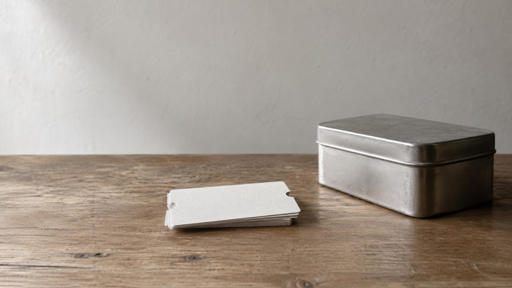 A small stack of blank paper coupons and a closed metal tin on a plain wooden counter.