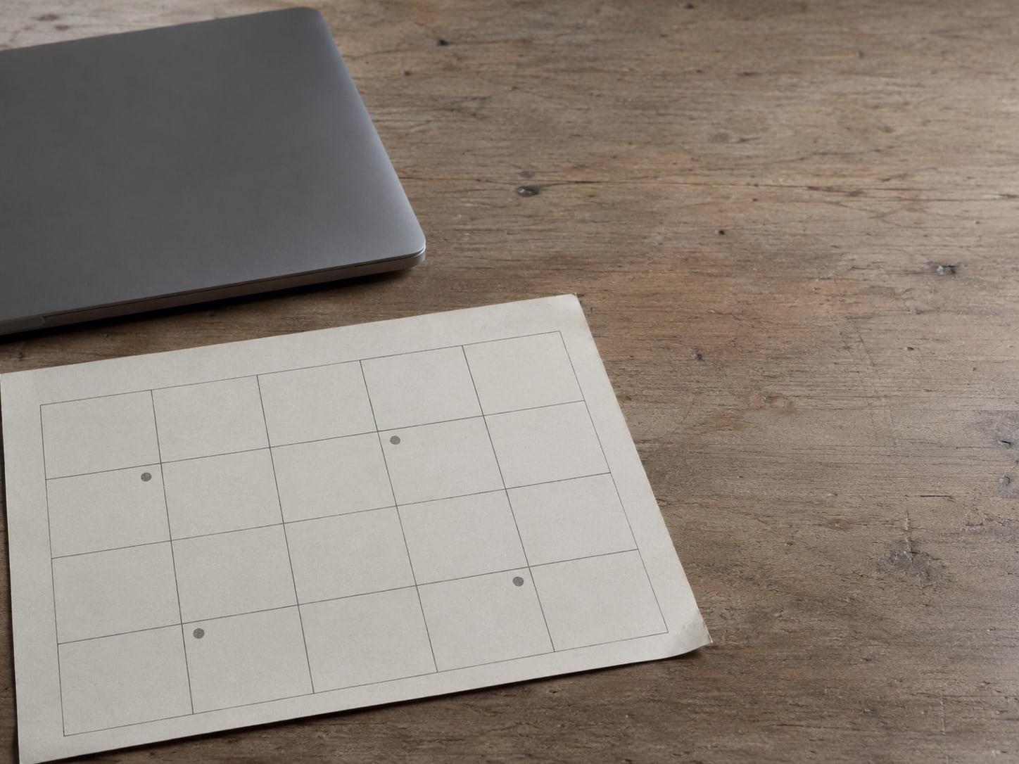 A calendar page with several blank squares marked by small pencil dots, lying flat beside a closed laptop.
