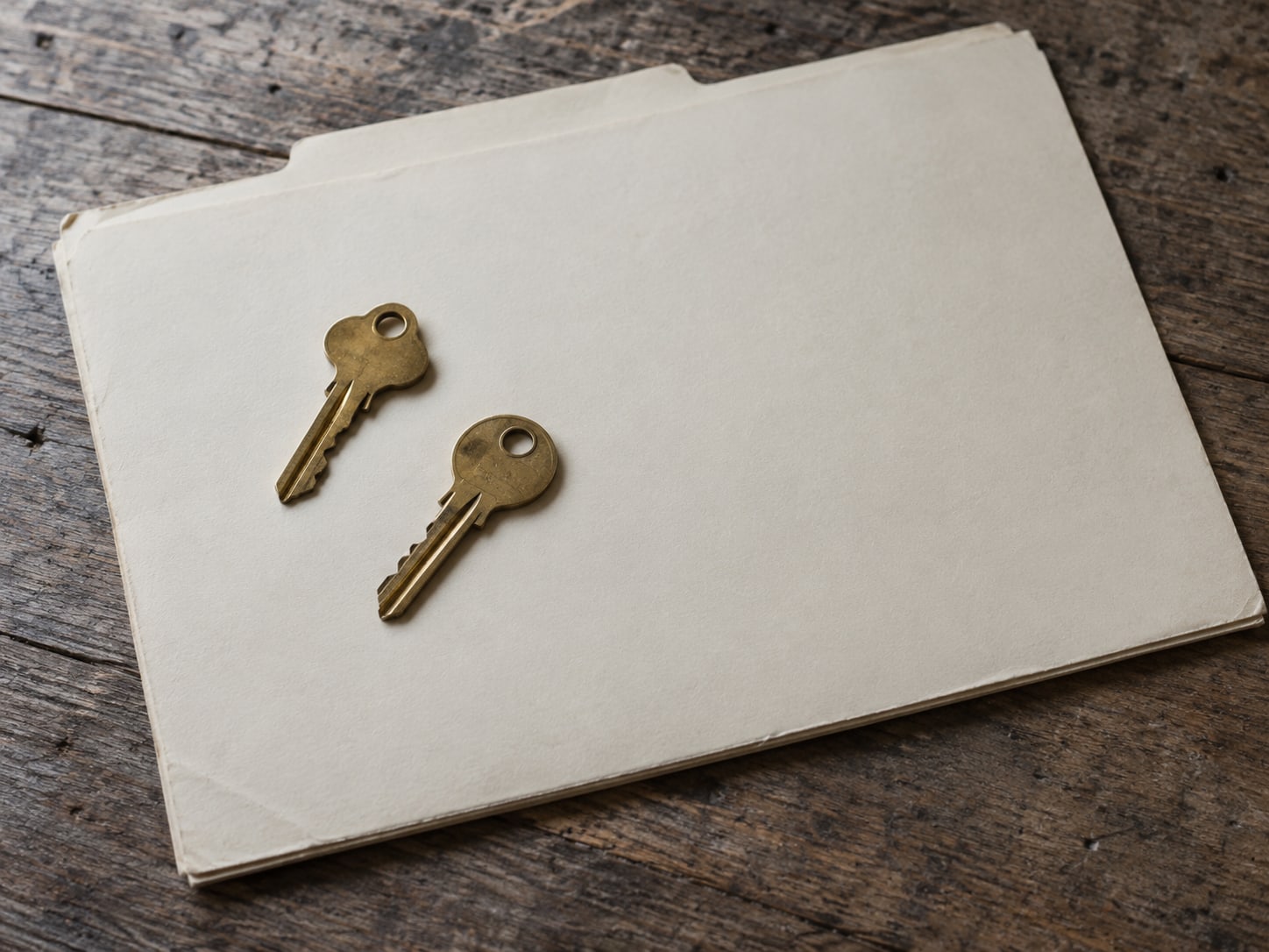 Two brass keys lying on a closed blank folder on a wooden counter.