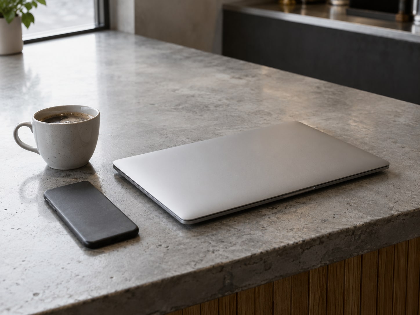 A closed laptop and a phone lying face down beside a coffee cup on a shop counter.
