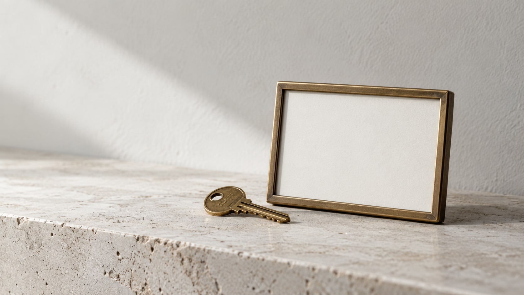 A brass key resting beside a small framed blank sign on a pale stone shelf.