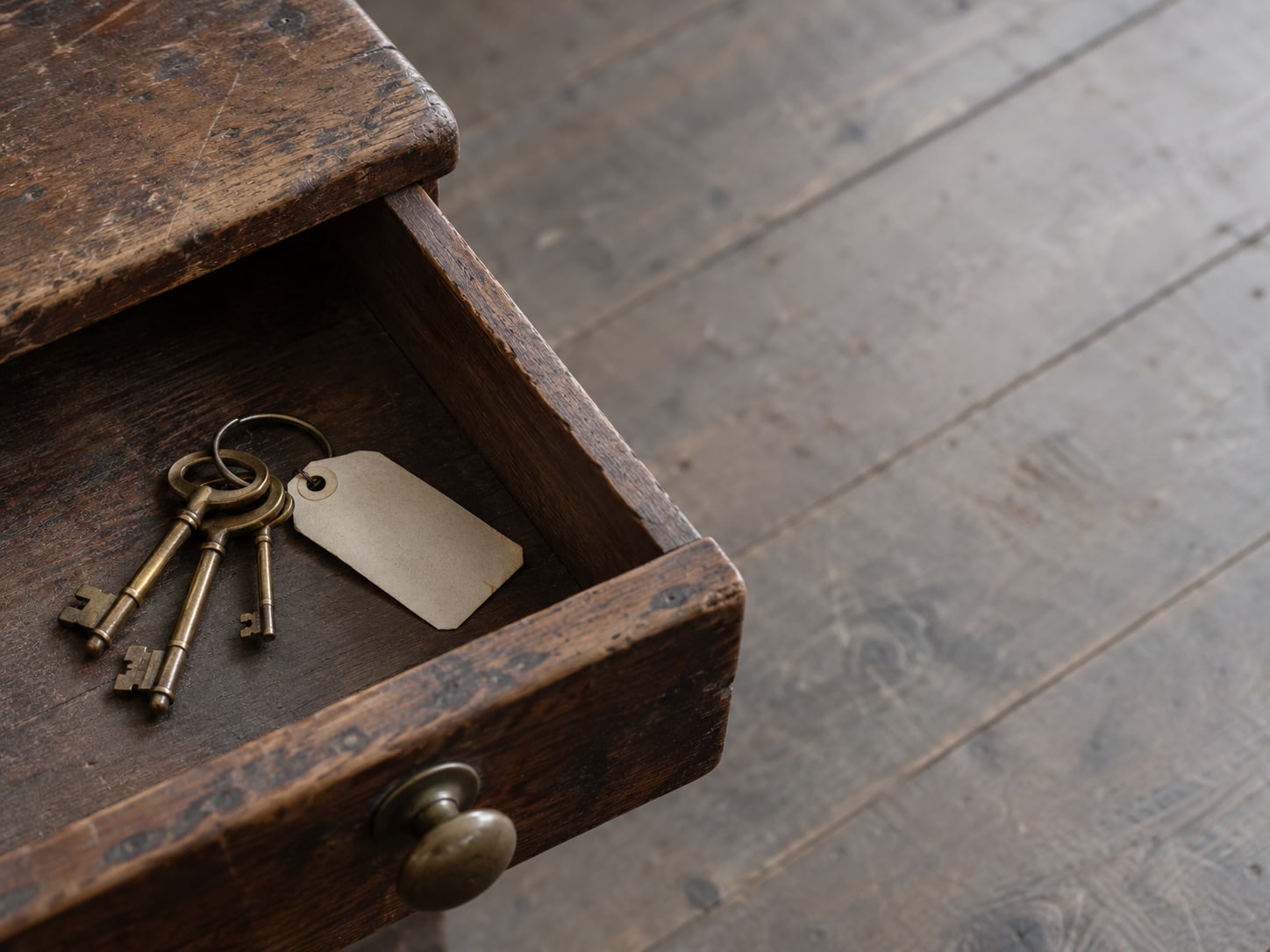 A wooden desk drawer pulled open with a ring of small brass keys and a blank paper tag beside it.