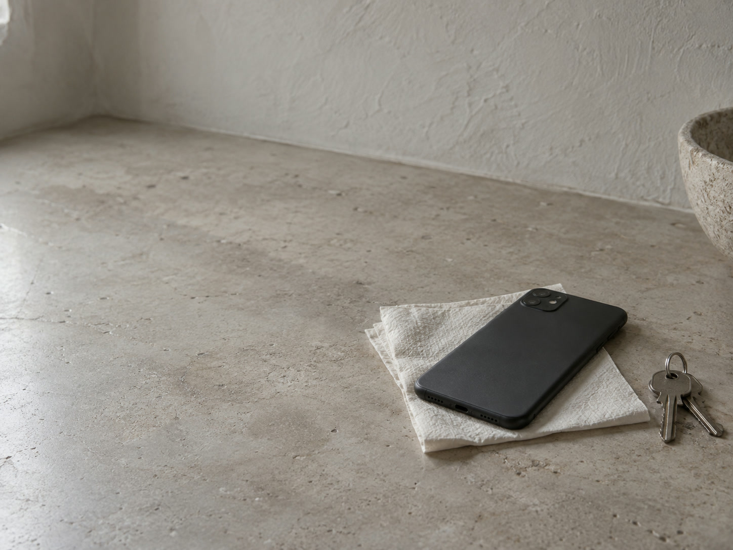 A face-down smartphone resting on a folded paper napkin next to a set of keys on a kitchen counter.