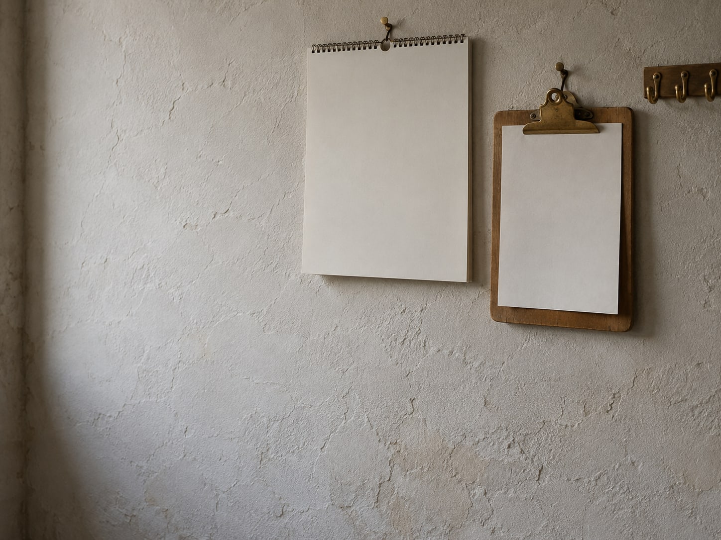 A wooden clipboard hanging from a hook beside a plain wall calendar and a row of empty key hooks.