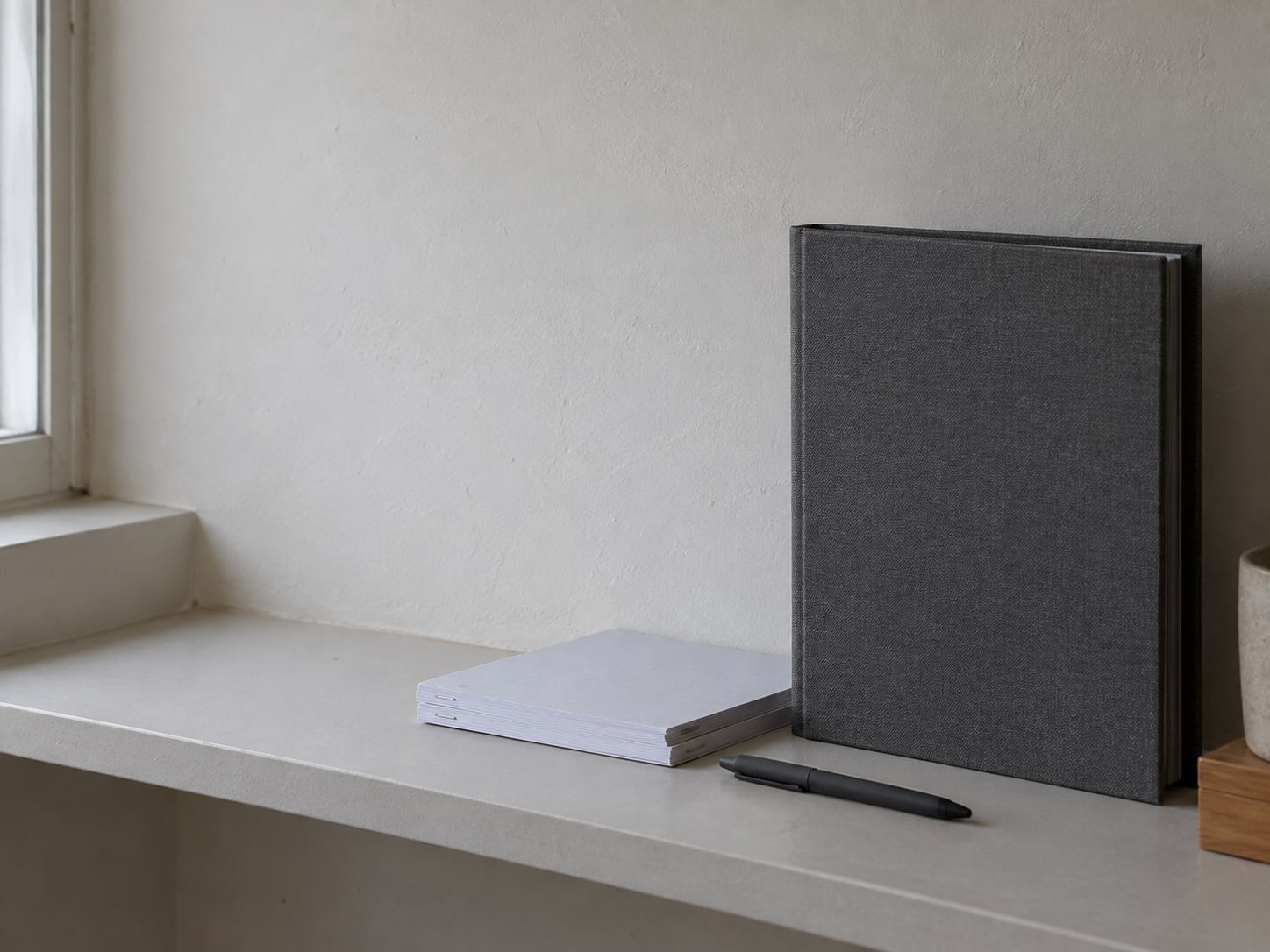 A closed binder with a plain pen and a small stack of stapled pages on a tidy office shelf.