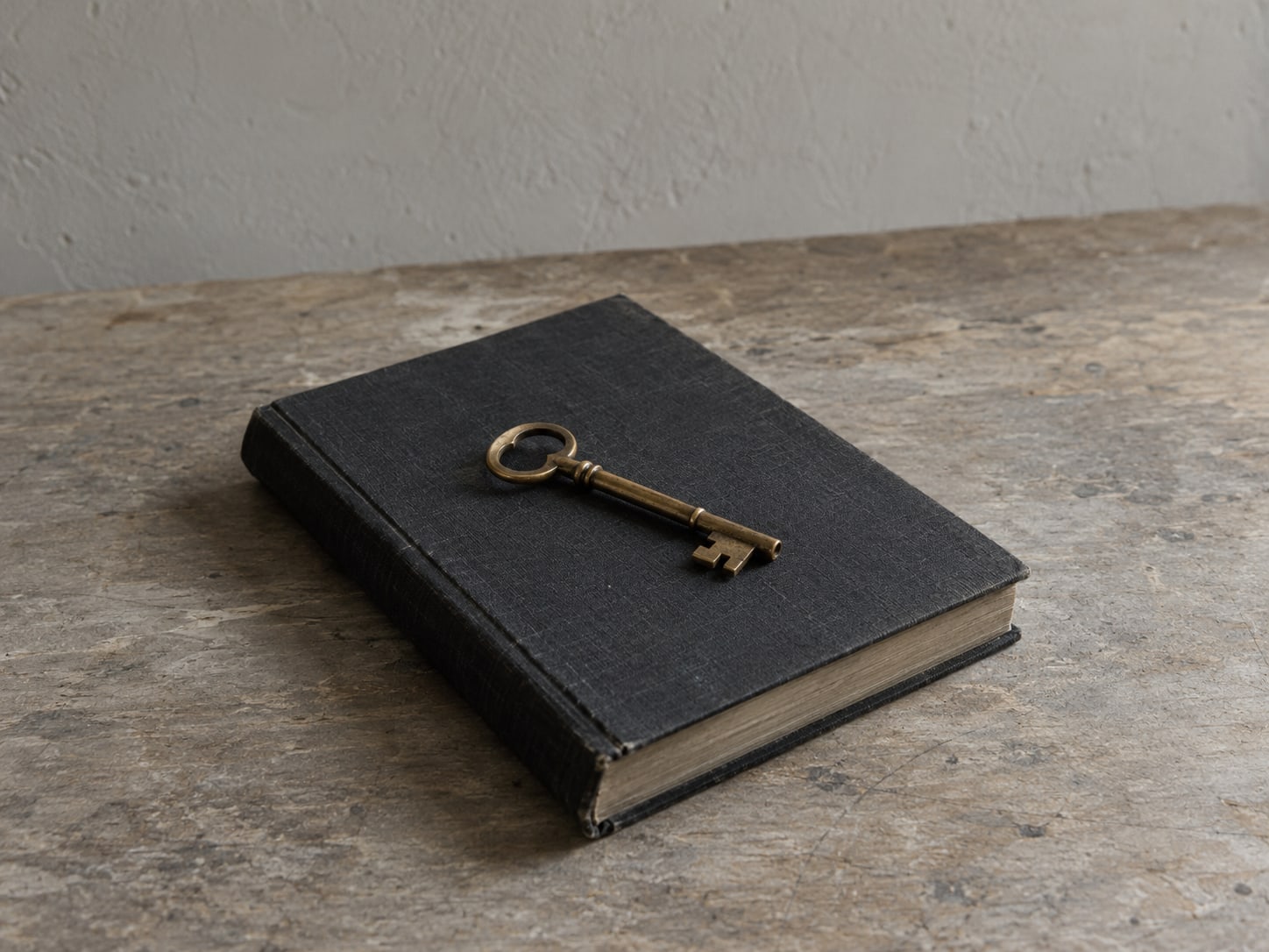 A single brass key lying on a closed ledger on a plain table.