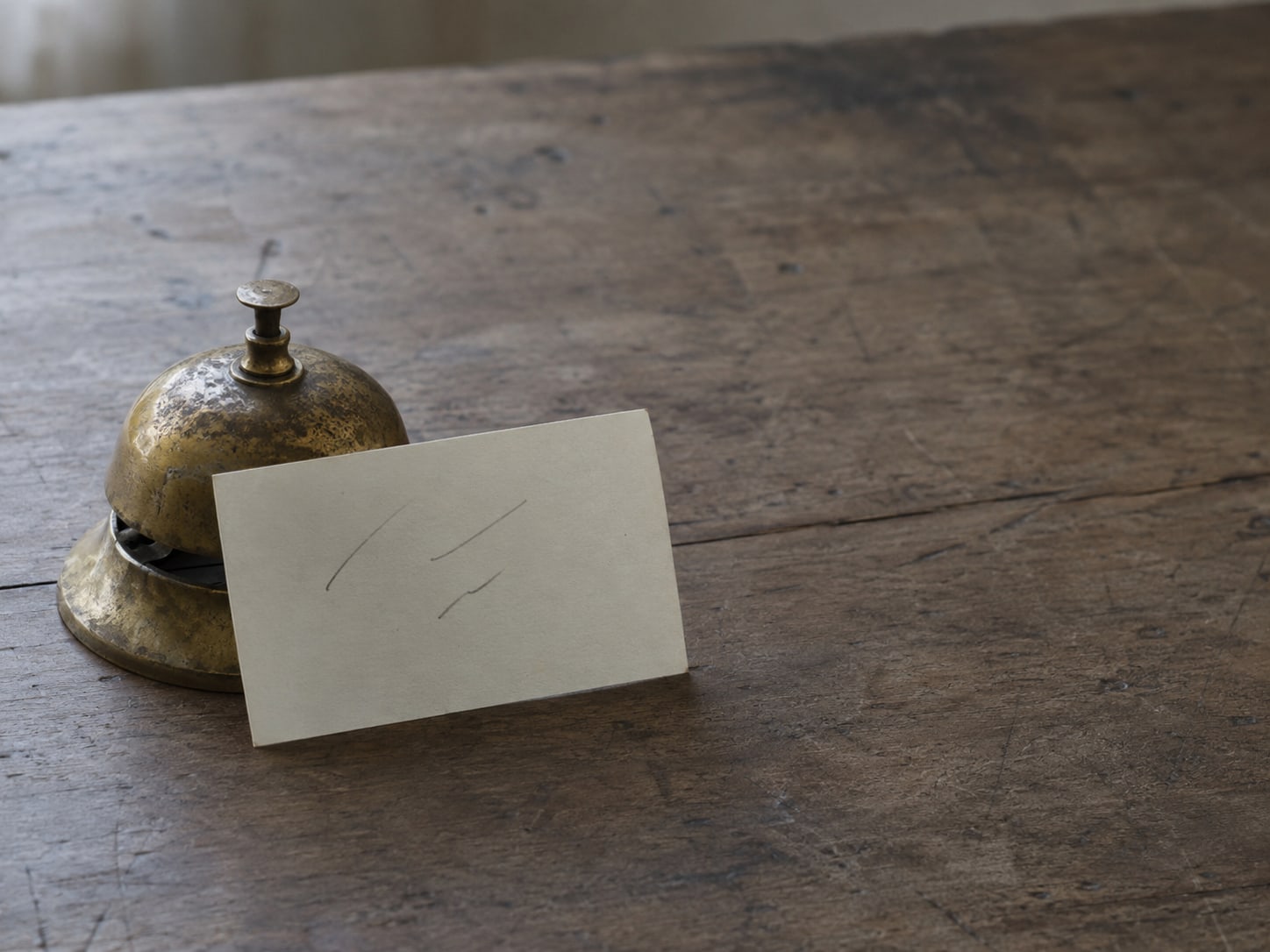 Una sola ficha con unas pocas líneas de lápiz ilegibles apoyada contra una pequeña campana de escritorio de latón sobre una mesa de madera lisa.