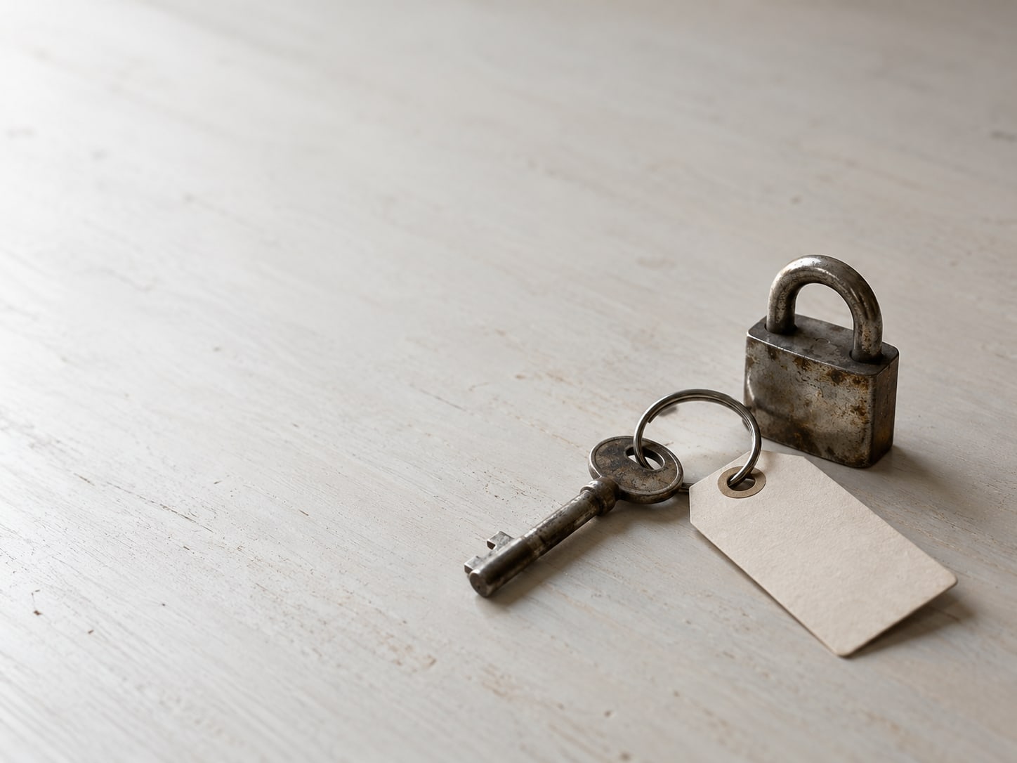 A single key on a ring resting beside a small padlock and a blank paper tag on a clean desk.