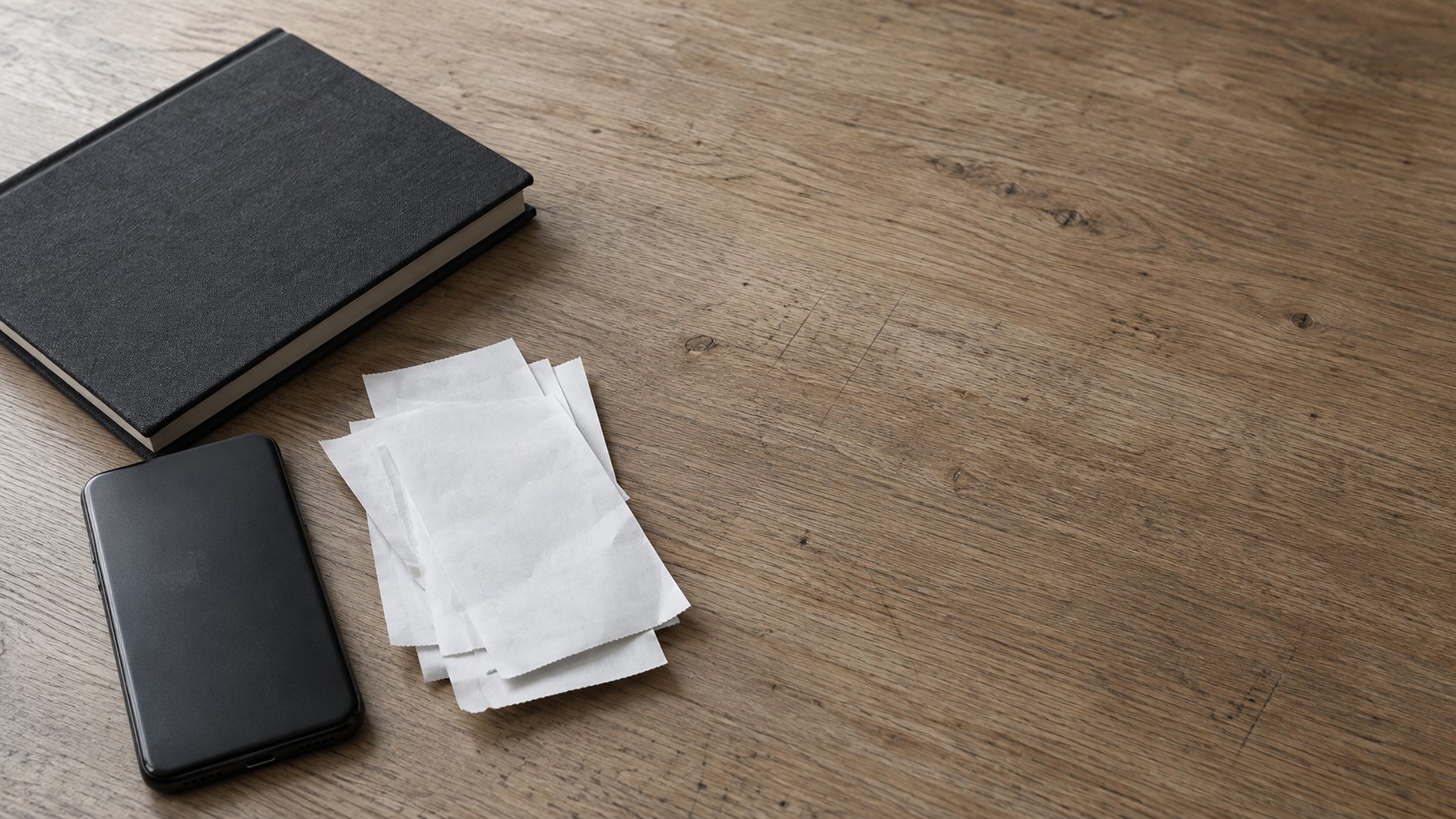A face-down phone beside a small pile of blank receipts and a closed ledger on a desk.