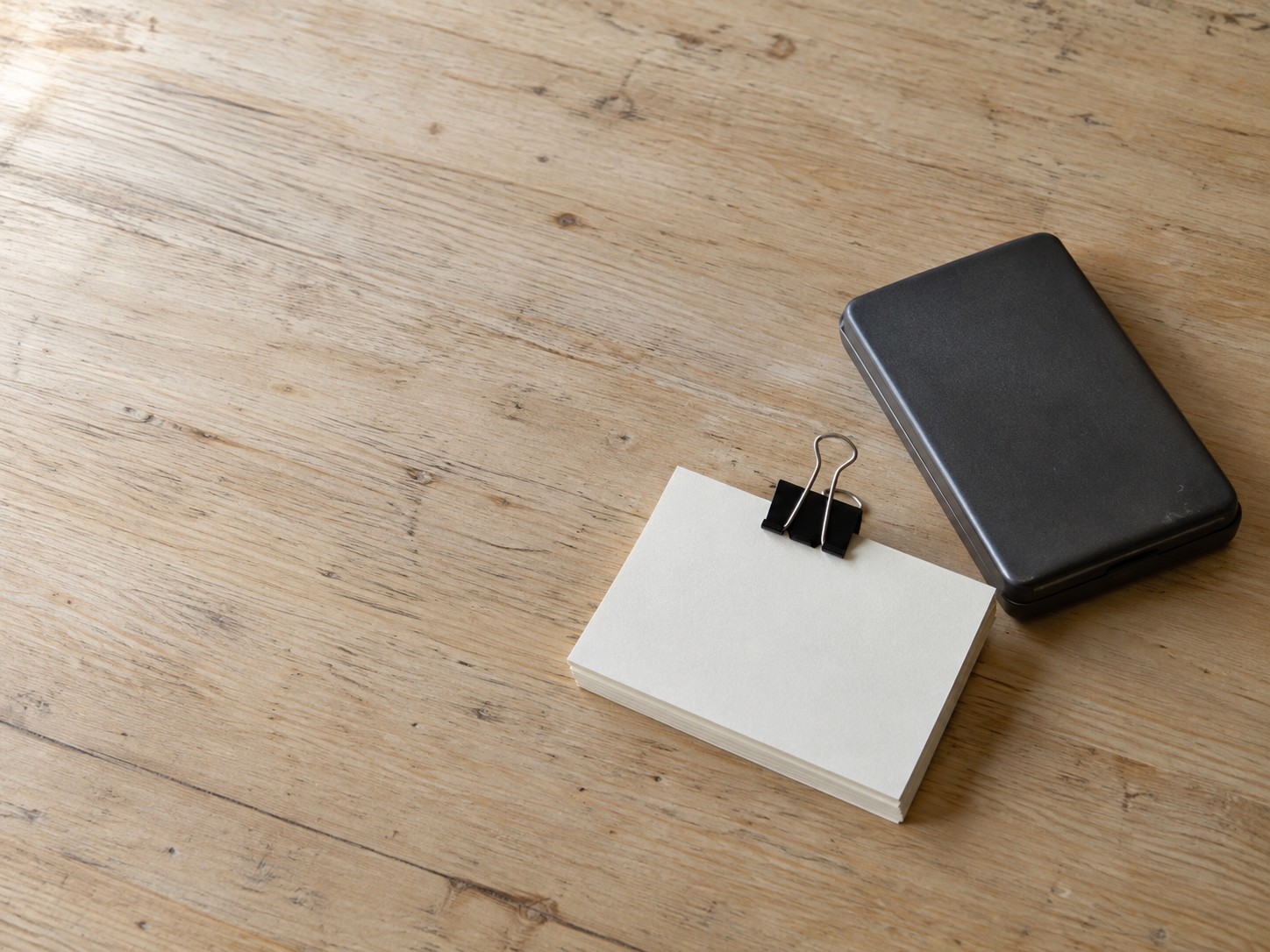A small stack of blank index cards held by a binder clip next to a closed calculator on a light wooden table.