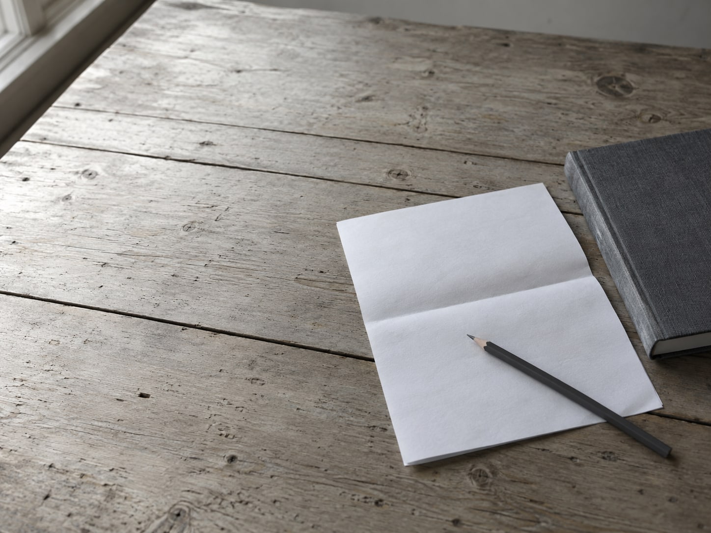 A pencil and a blank folded checklist on a wooden table next to a closed notebook.