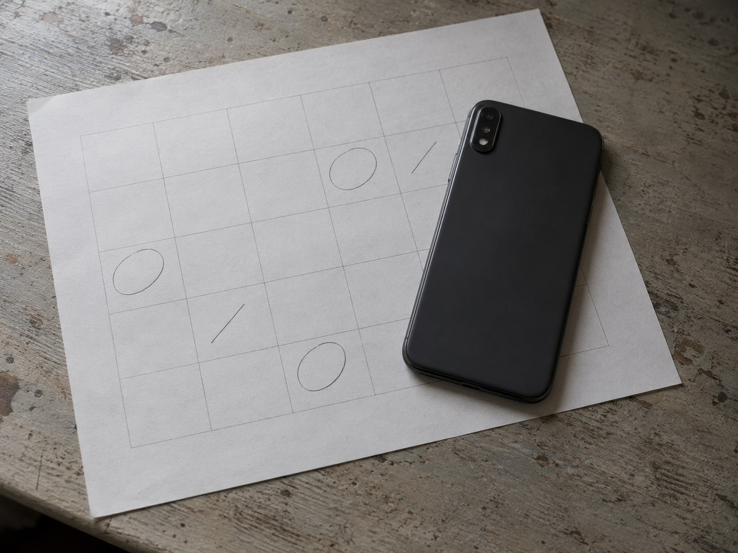 A paper calendar page with a few pencil marks and a closed phone resting on top of it.