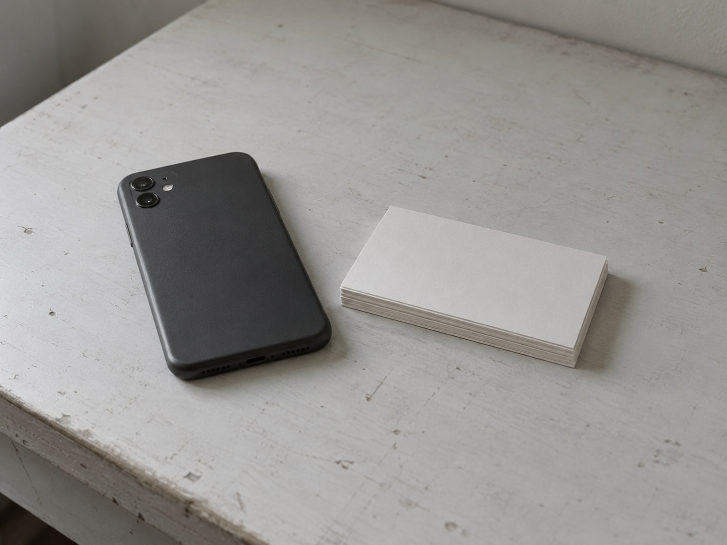 A phone lying face down on a desk next to a small stack of index cards with unreadable pencil marks.