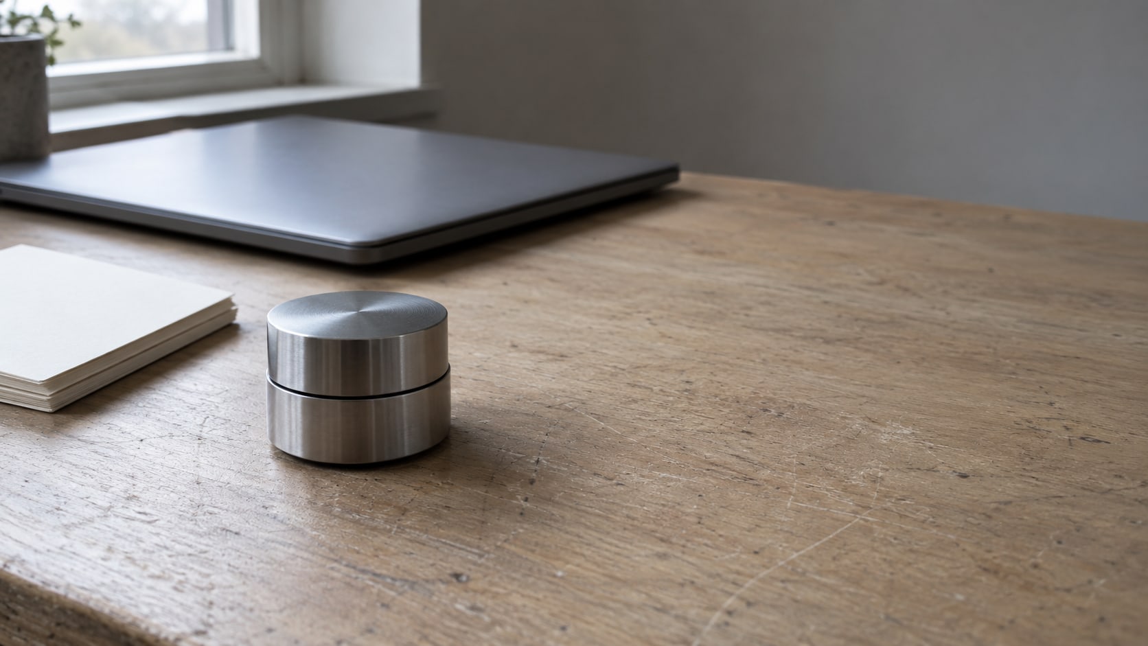 A kitchen timer, a closed laptop and a small stack of blank notepaper on a clean wooden desk.