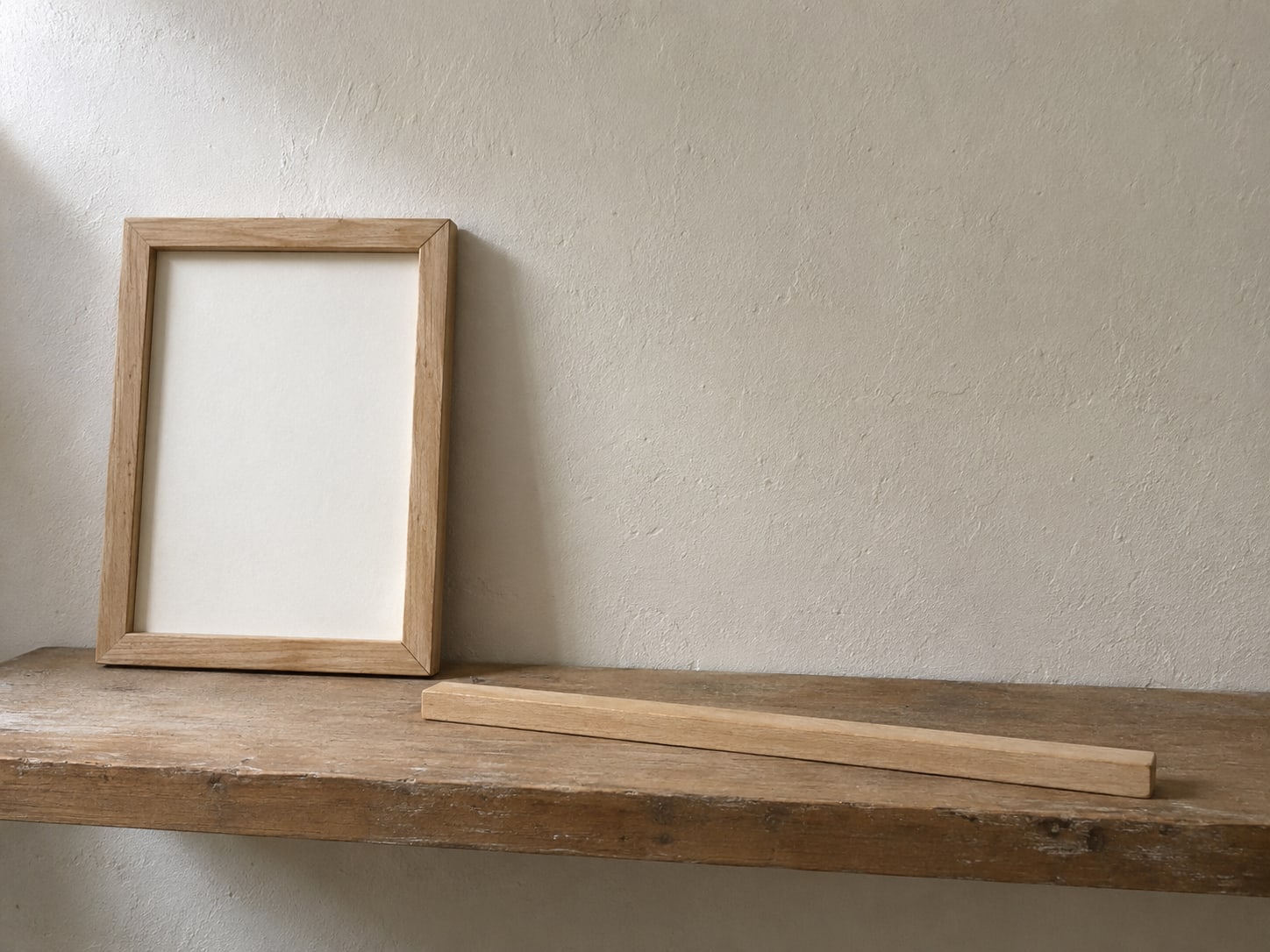 A small wooden photo frame leaning against a wall next to an empty shelf with a ruler laid across it.