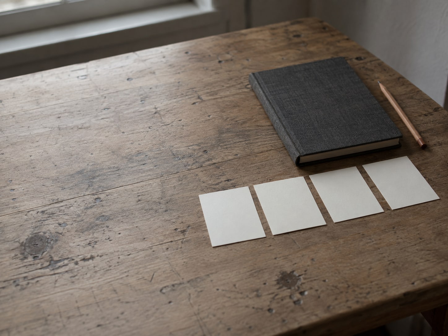 Cuatro fichas en blanco en fila sobre un escritorio de madera, junto a una libreta cerrada y un lápiz.